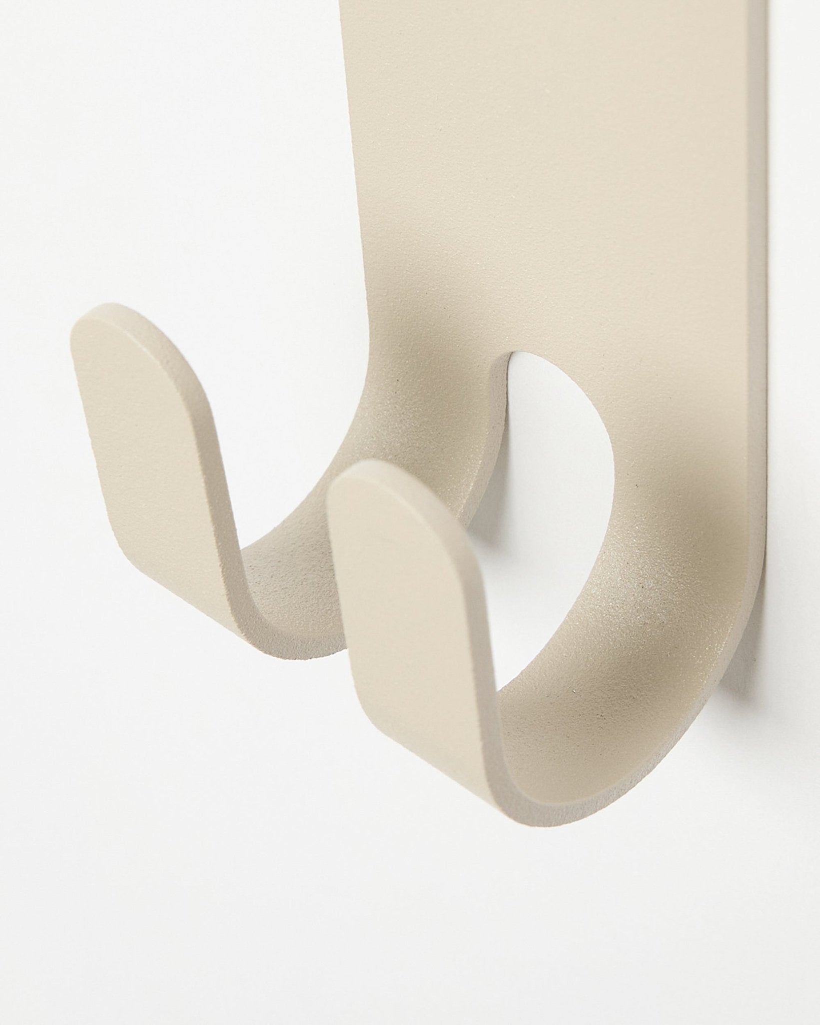 Närbild av Norr Double Hanger i beige från WoodUpp, en minimalistisk metallkrok för ytterkläder monterad på en ljus-colored Akustikpanel.