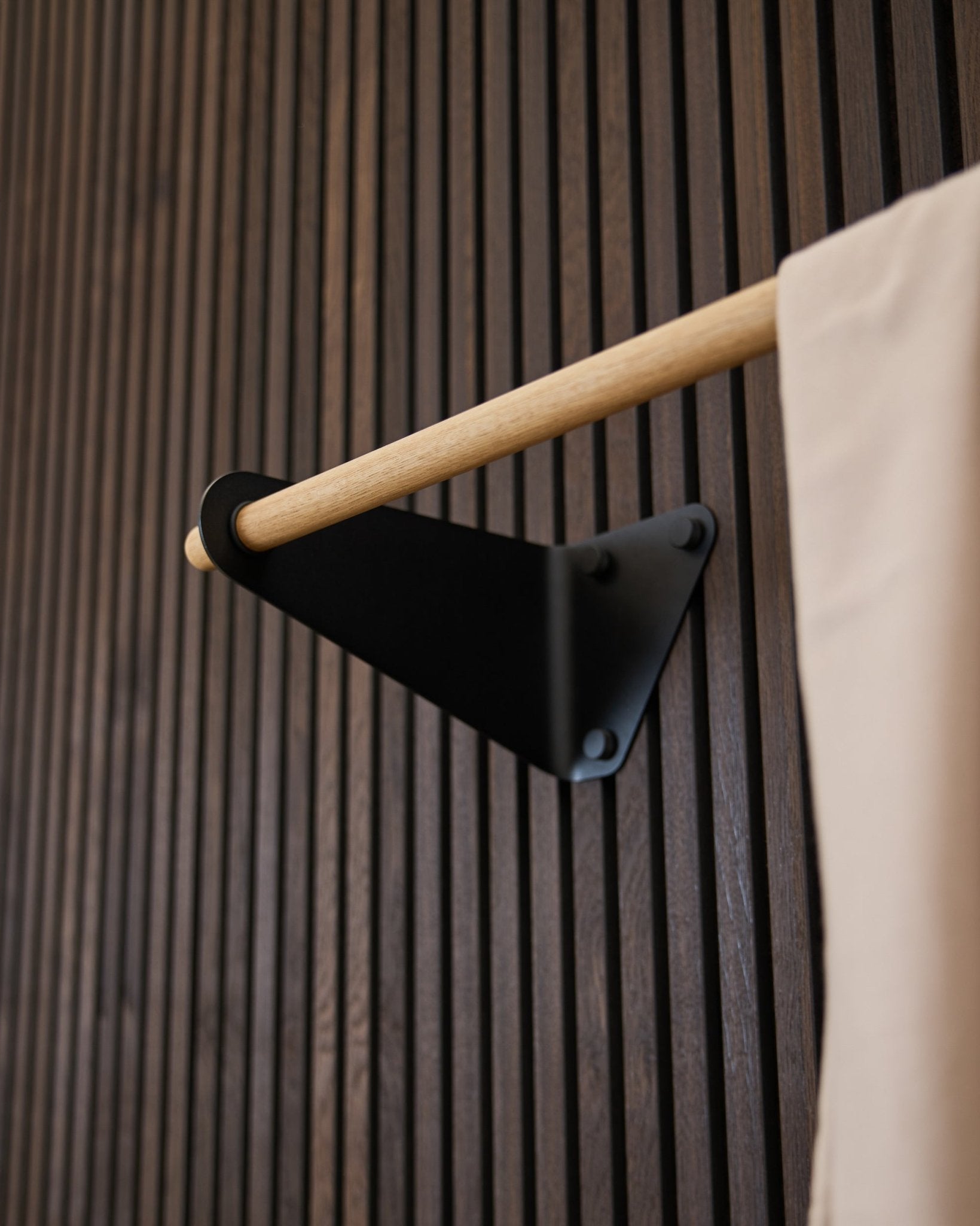 Linn Coat Rail från WoodUpp i black (115,9 cm), monterad på en mörk räfflad Akupanel Akustikpanel, med textildetalj i beige och konsol i black.