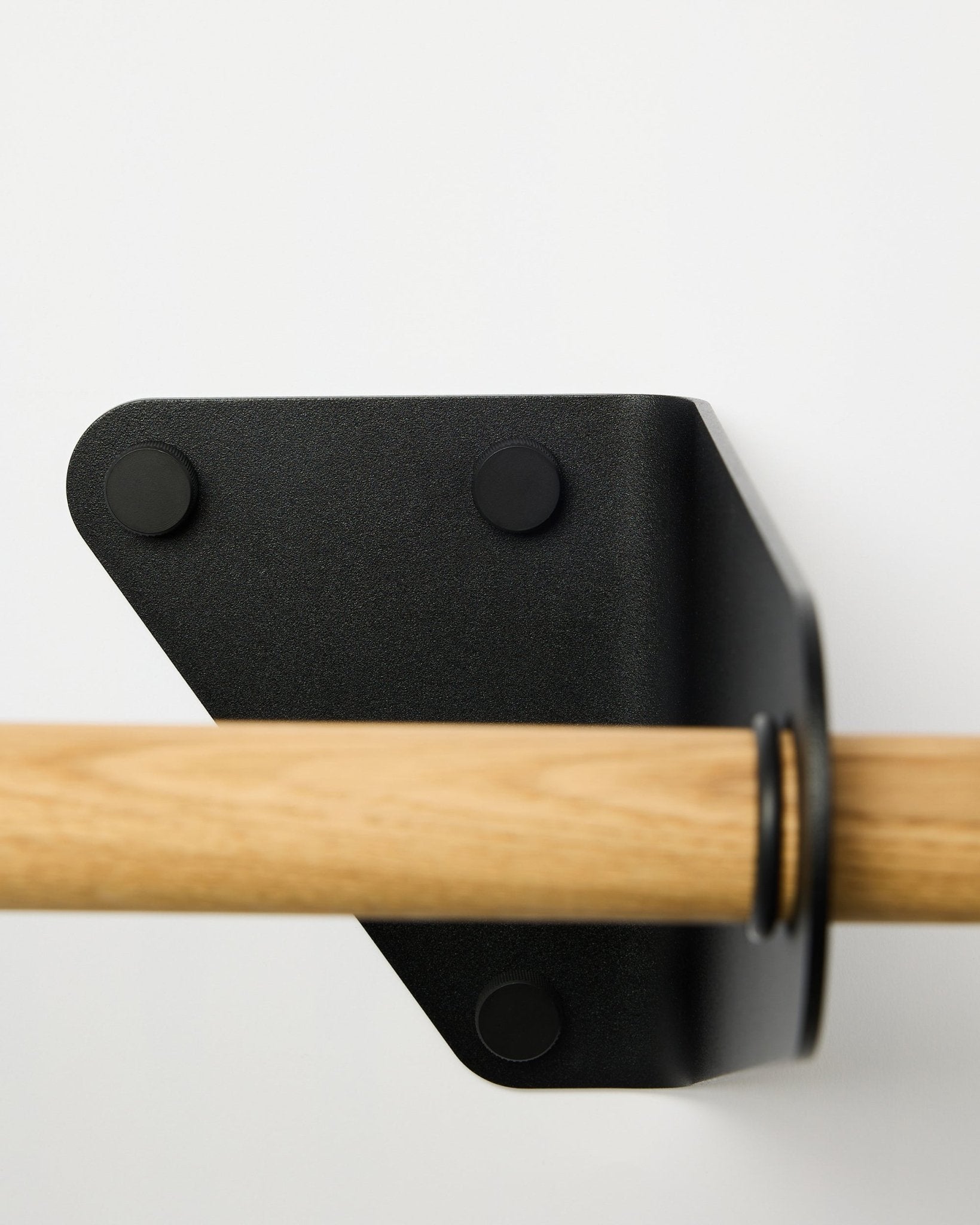 Närbild på WoodUpp Linn Coat Rail i black, 115,9 cm, monterad på en vit vägg med en triangelformad metallkonsol, visad som en del av nordiska akustiktillbehör.
