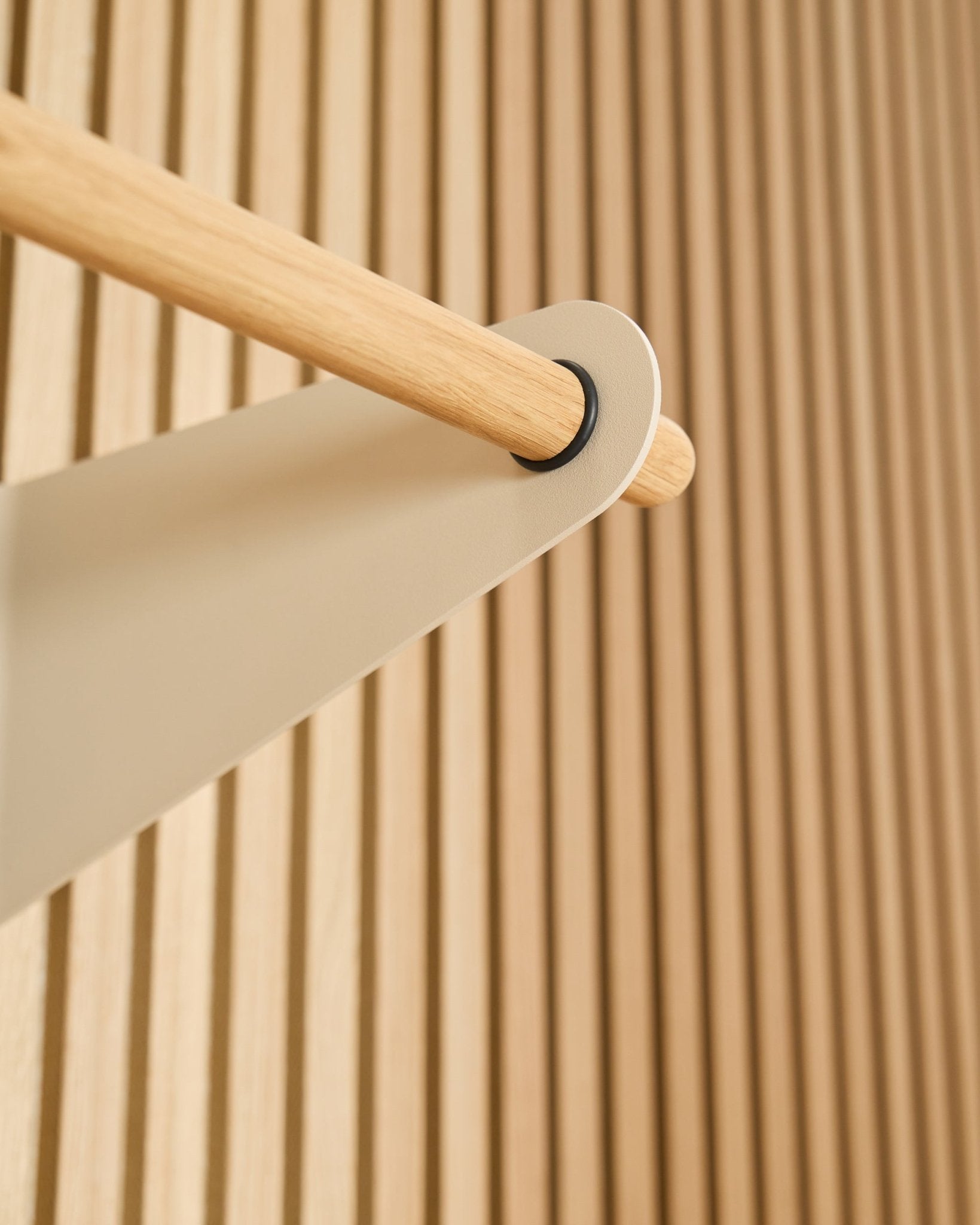 Närbild av WoodUpp Linn klädstång i beige (75,9 cm), monterad på ett beige metallfäste mot en texturerad Akupanel akustisk ribbpanel.