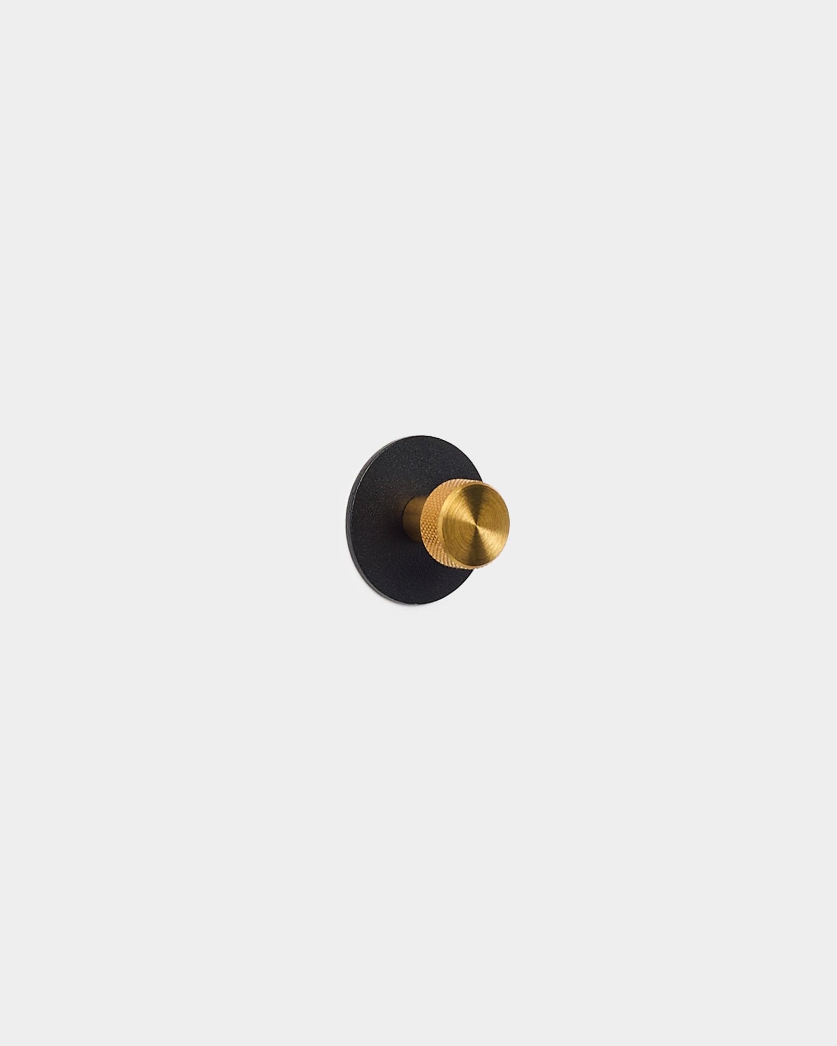 Guldfärgad klädkrok monterad på en black Akupanel Akustikpanel bas, tillverkad i pulverlackerat steel av WoodUpp.