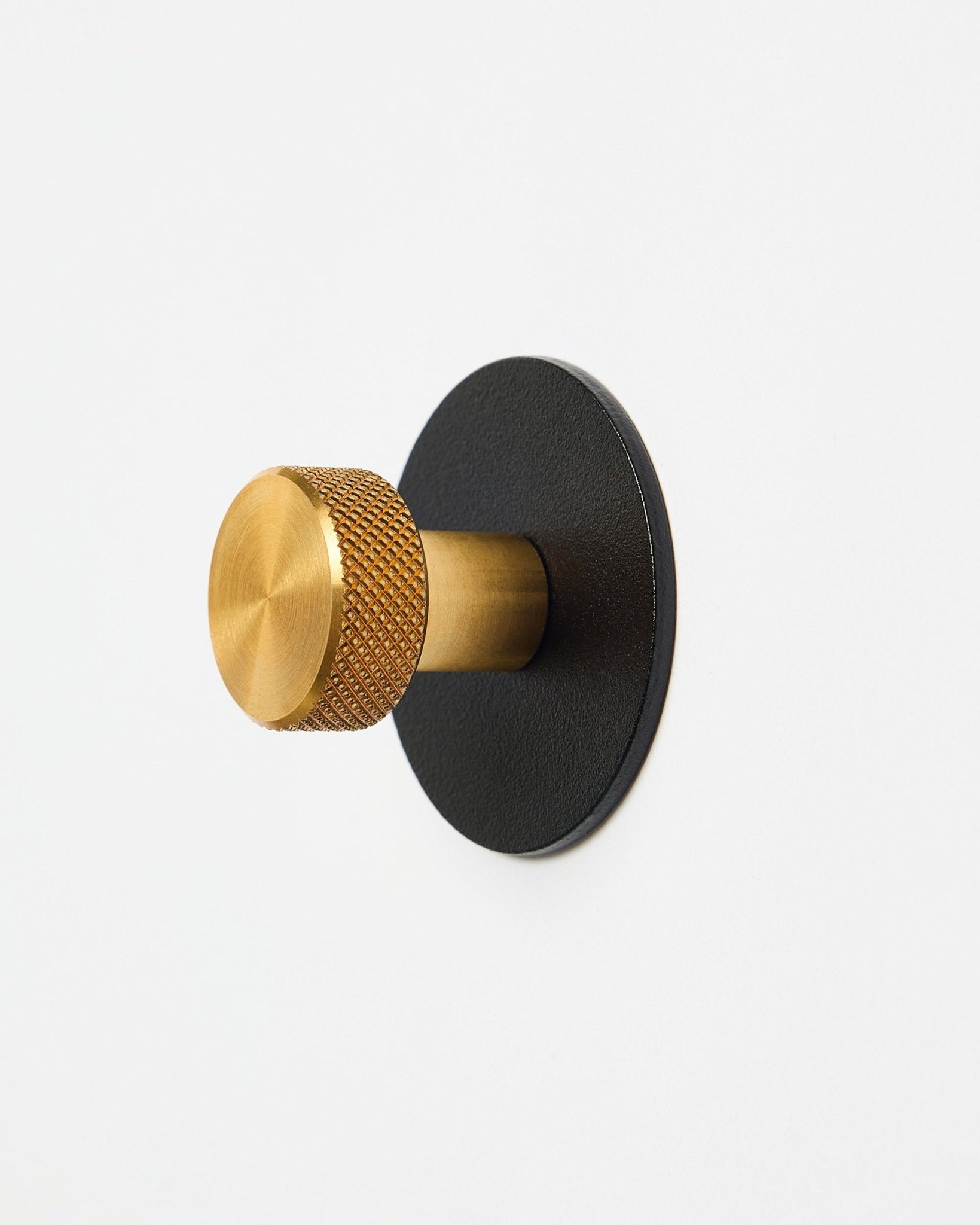 Norr Coat Hook X1 från WoodUpp med en texturerad brass knopp och black pulverlackerad steel bas, tillbehör för Akupanel, visad mot vit bakgrund.