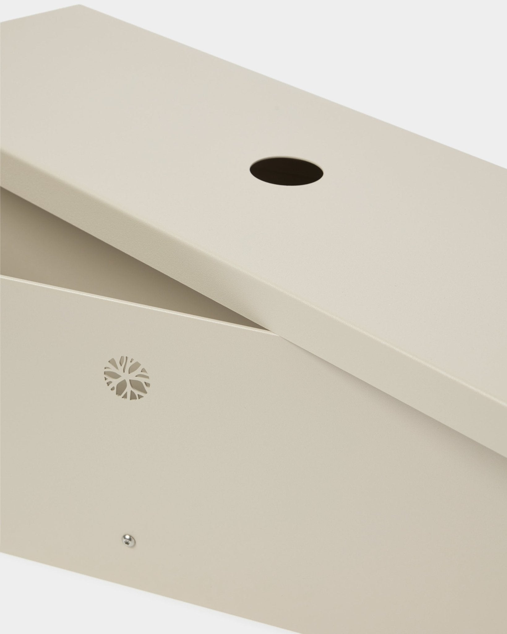 Nell | Metal Box / BM2, Beige från WoodUpp är tillverkad i pulverlackerad steel och har ett snedställt lock, rund öppning och ett diskret emblem på sidan.