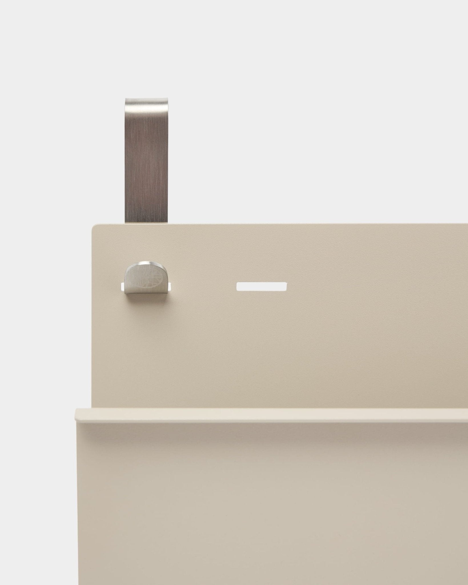Närbild av WoodUpp Nell Magazine Storage i beige pulverlackerad steel med hylla, slits, bult och böjt handtag; fungerar som rumsavdelare eller tidningshållare.