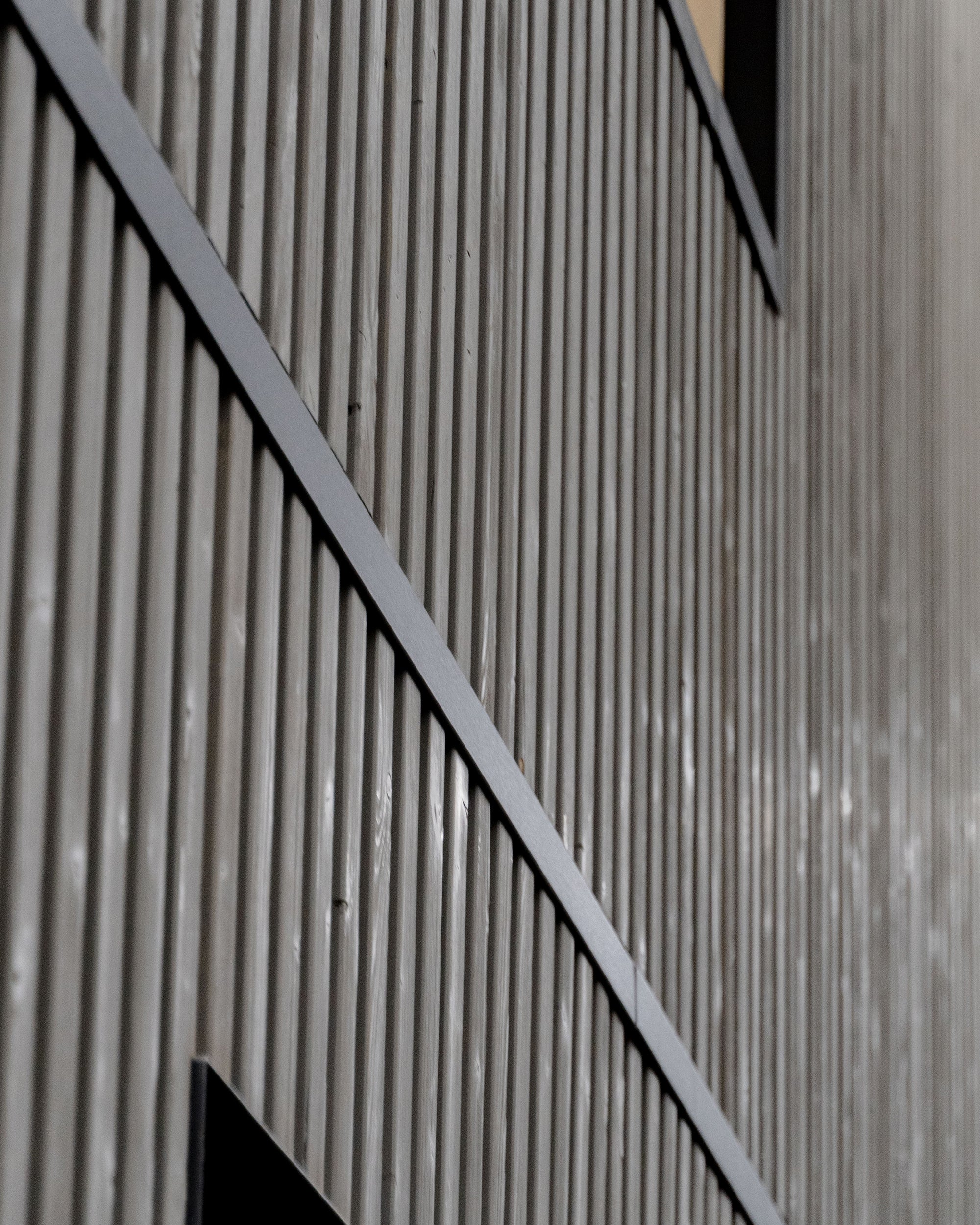Aluwood aluminium slat cladding on a grey exterior facade with black curved metal detail