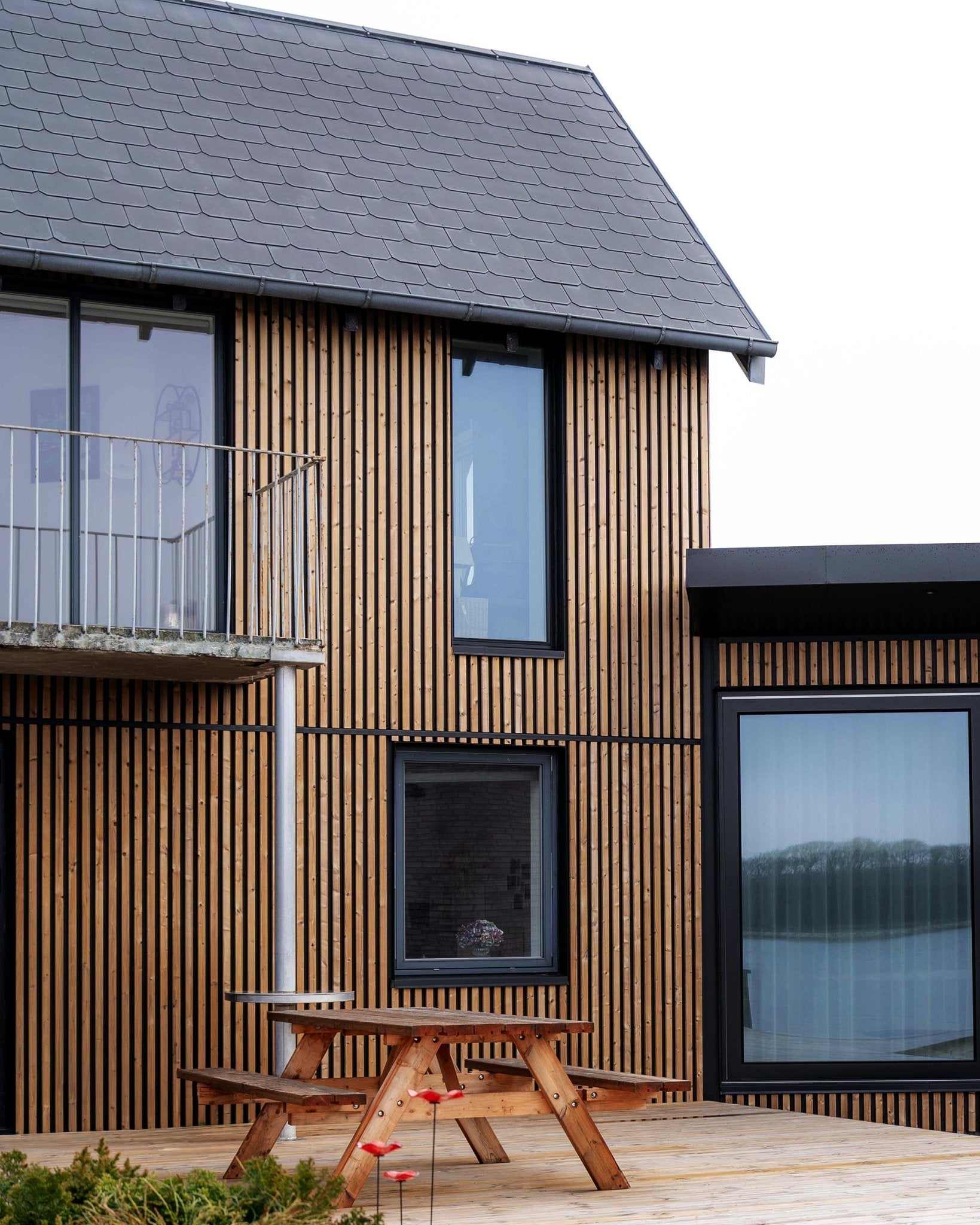 Modernt hus med WoodUpp Aluwood fasadpaneler i Oiled Brown, med large fönster, en balkong och en altan med ett picknickbord i trä.