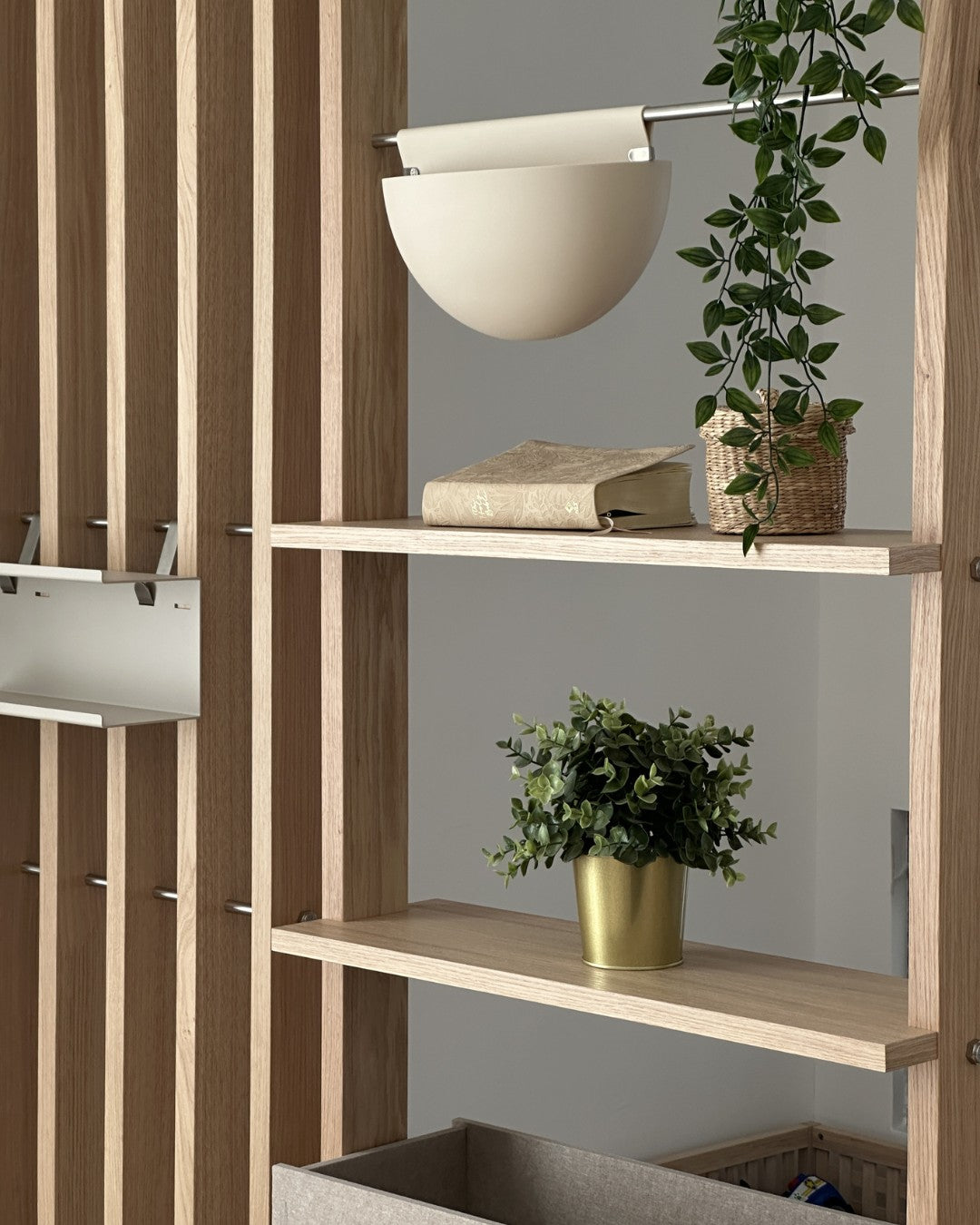 Wooden room divider unit with books, plants, and a basket against a gray wall.