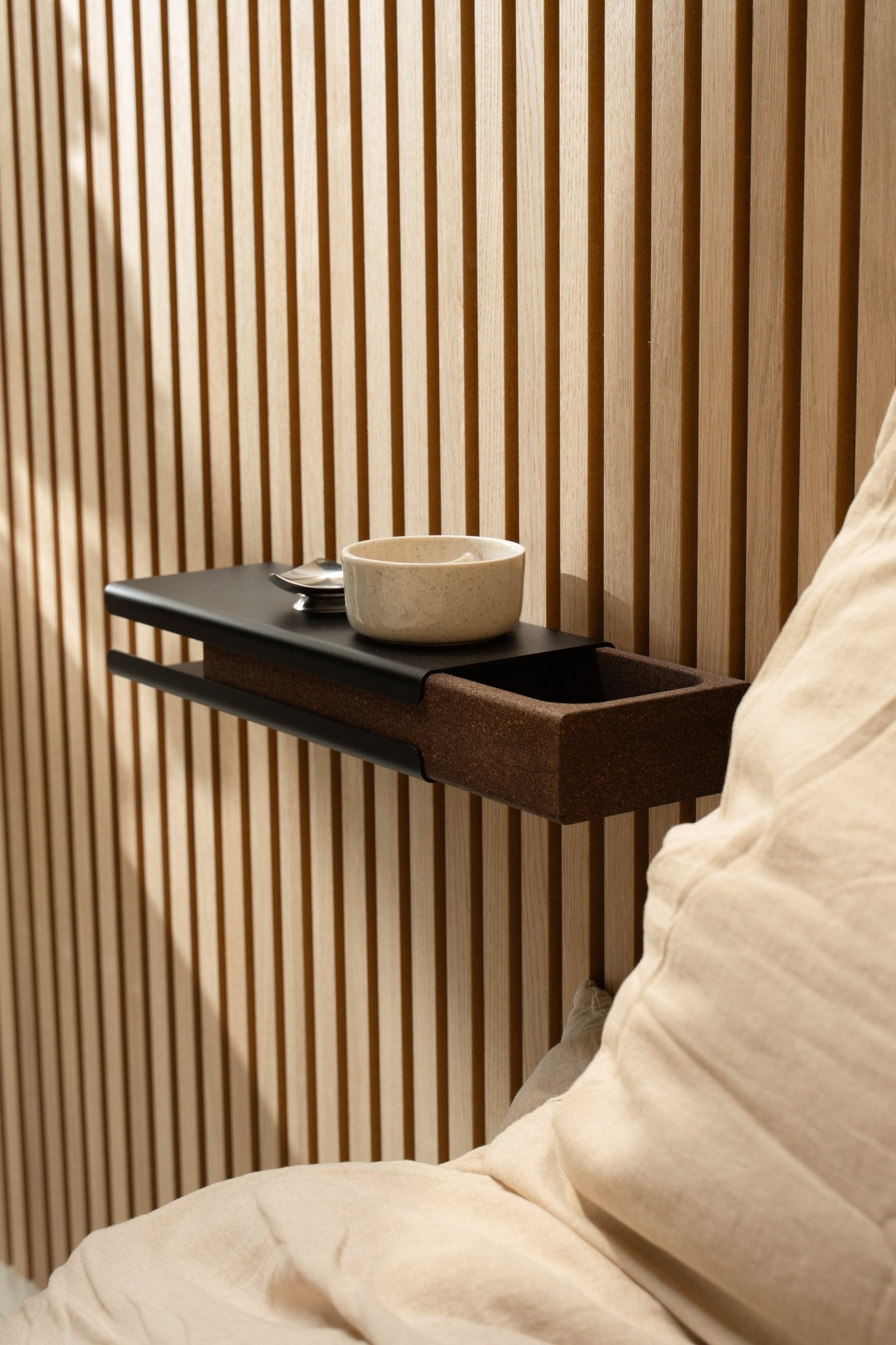 Minimalistisk vägghylla med en keramisk skål och WoodUpp Norr Key Tray intill en beige kudde och Akupanel Akustikpanel, upplyst av mjukt naturligt ljus.