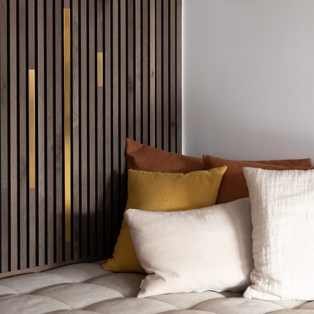 Krämfärgade, gula och bruna kuddar i en beige tuftad soffa bredvid en modern akustisk slatwallpanel med guldaccenter för en mysig, modern miljö.