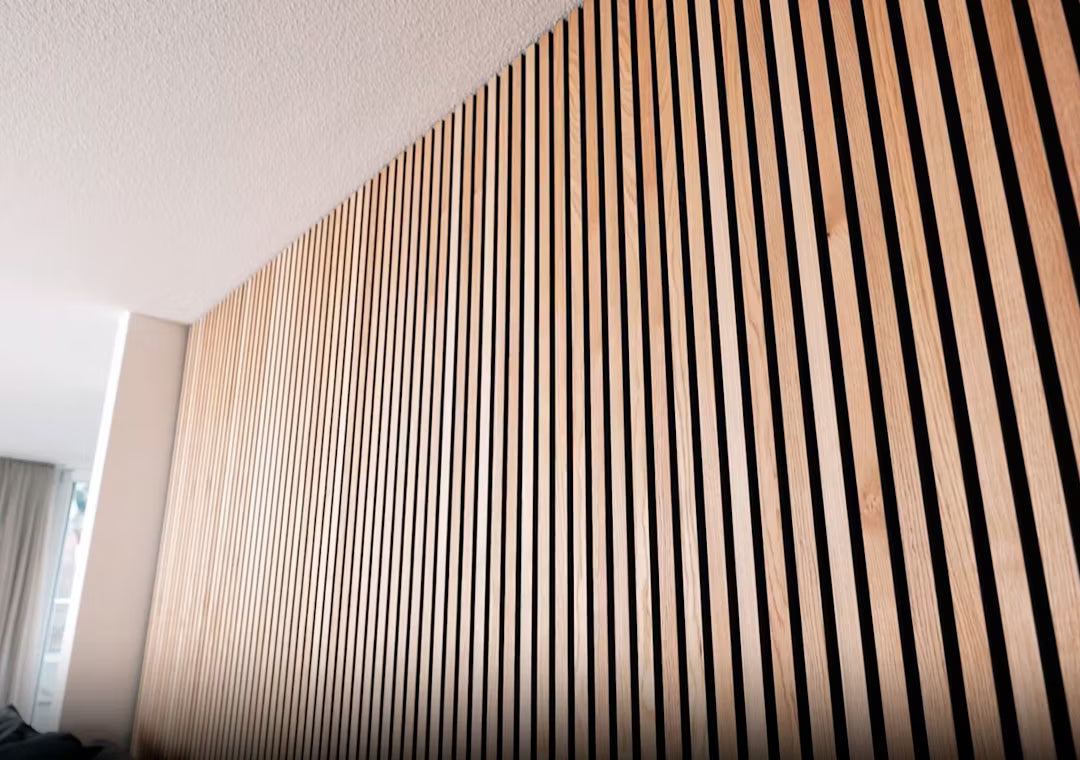 Närbild av Akupanel akustisk träpanel med vertikala trälameller i randigt mönster, monterad på en innervägg under ett vitt tak.