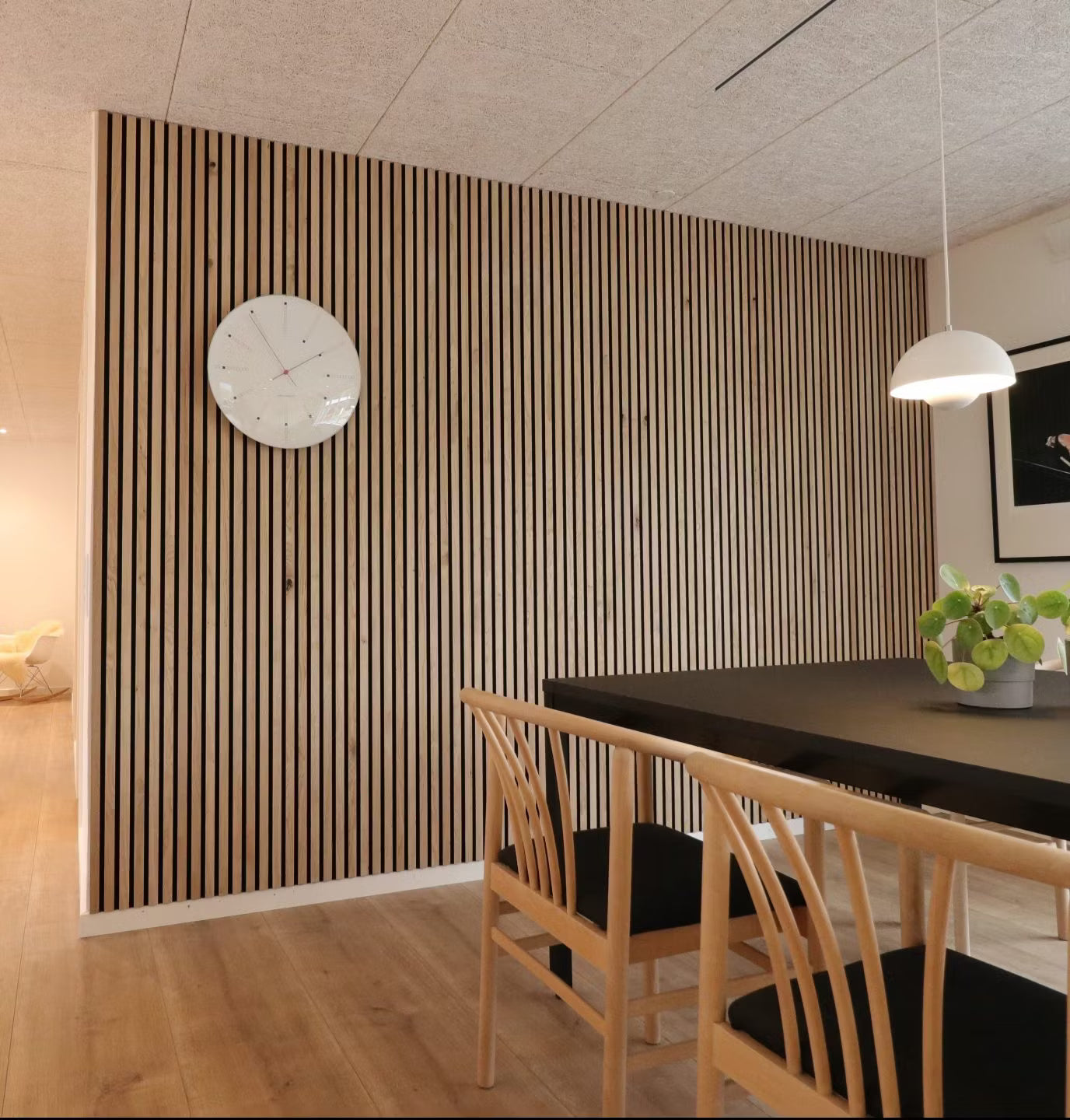 Modern matsal med en accentvägg med akustiska träribbor från Akupanel, svart bord, trästolar med svarta sitsar och en krukväxt i mitten.