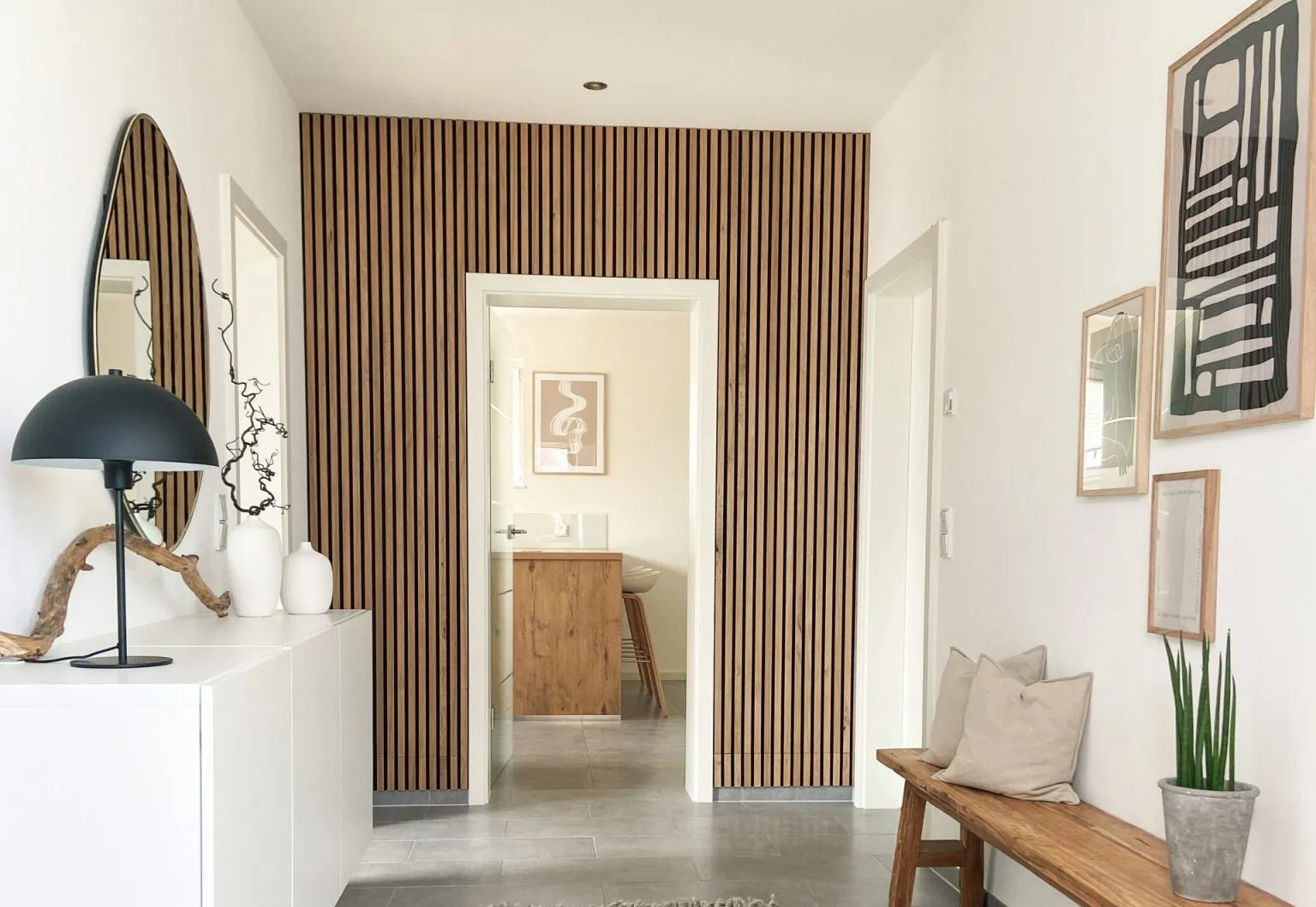 En modern hall med en akustisk accentvägg med Akupanel-träribbor, vita väggar, en kuddbänk och minimalistisk inredning.