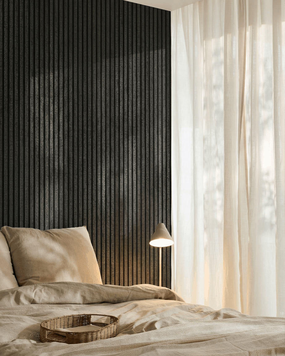 Mysigt sovrum med beige sängkläder, en bricka i rotting, vit lampa, skira gardiner och en WoodUpp Akupanel akustikpanel i trä i charcoal monterad på väggen.