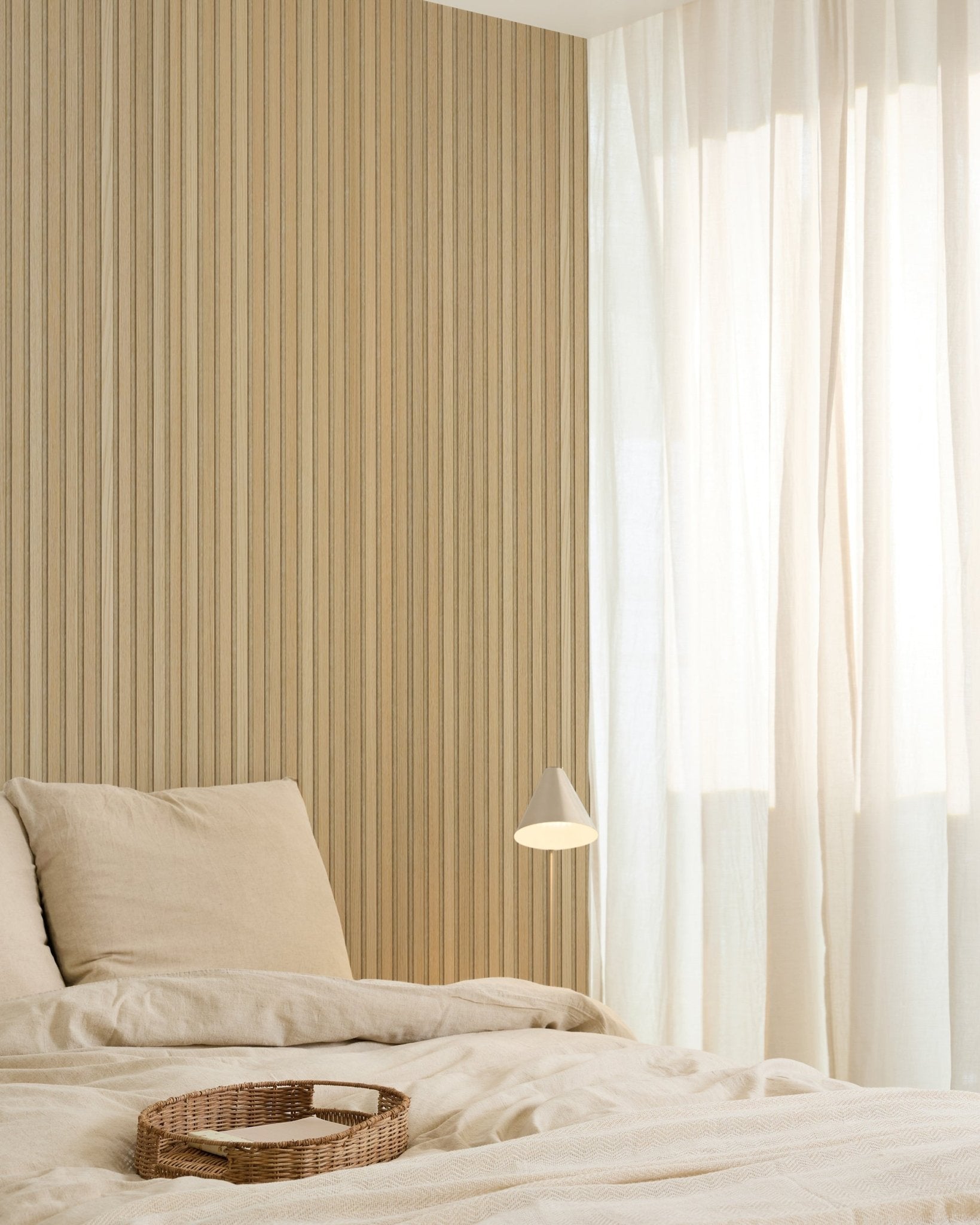 Minimalistiskt sovrum med beige sängkläder, en bricka i rotting, modern vägglampa, Akupanel accentvägg i akustiska träpaneler och skira gardiner som släpper in ett mjukt naturligt ljus.