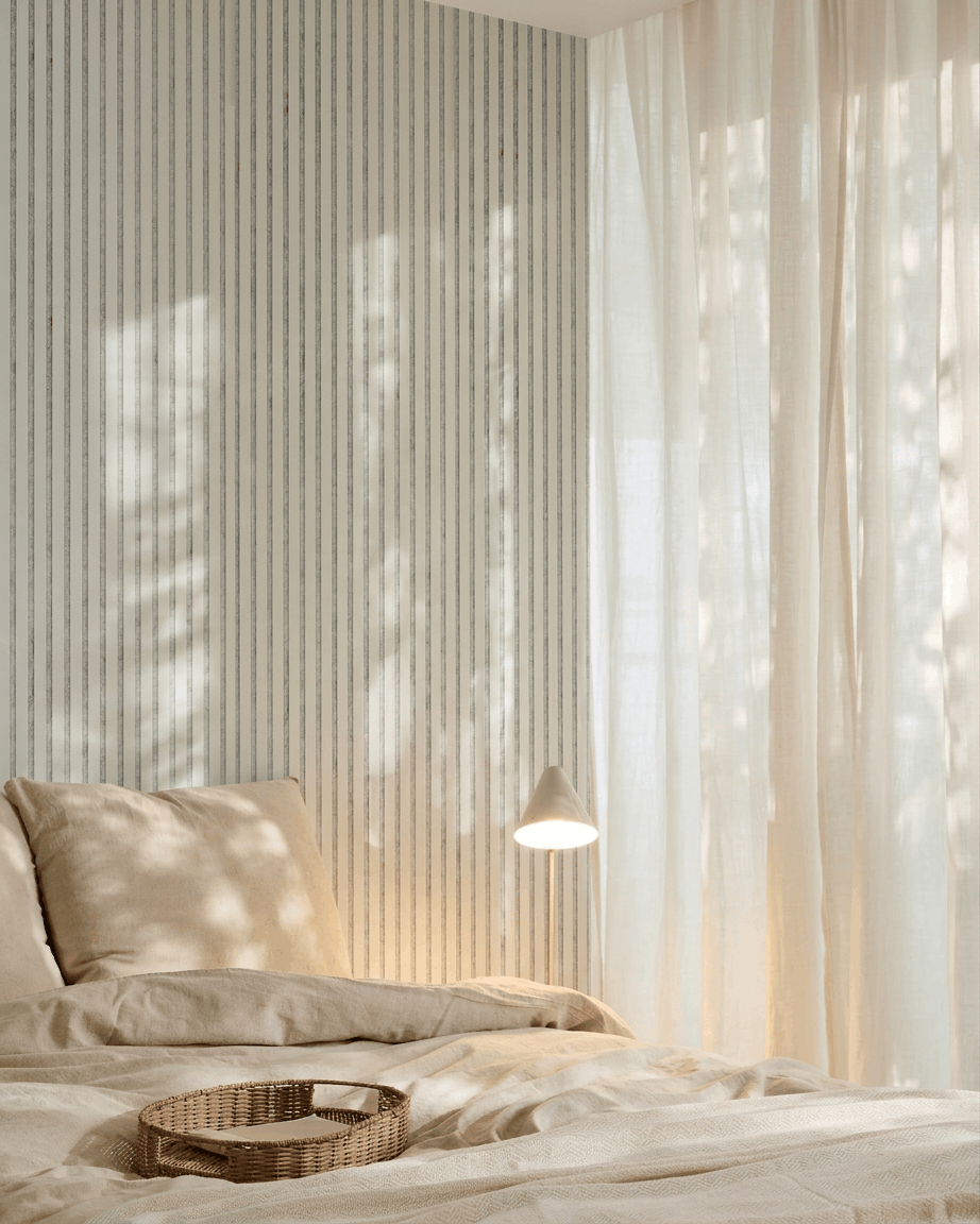 Minimalistiskt sovrum med beige sängkläder, en bricka i rotting, randig tapet och en WoodUpp Akupanel akustisk träpanel i Snow Grey Felt för ljudabsorption.