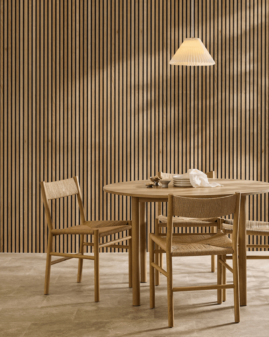 Minimalistisk matplats med ett runt bord, flätade stolar och WoodUpp Akupanel akustisk ribbväggspanel i Rustic Natural Oak som en nordisk väggaccent.