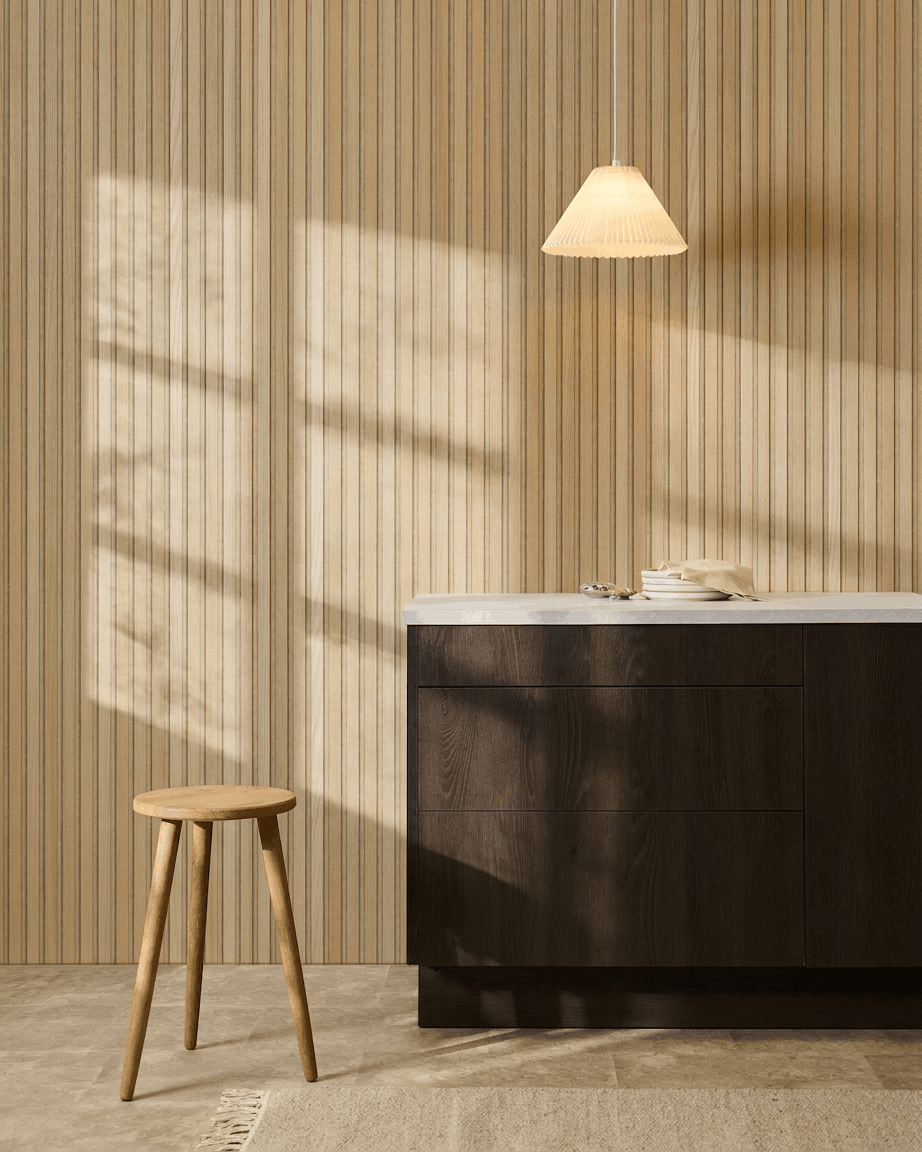 Skandinaviskt kök med WoodUpp Akupanel Classic Oak akustisk ribbväggspanel, mörka träskåp, träpall, pendellampa och solljus som kastar skuggor.
