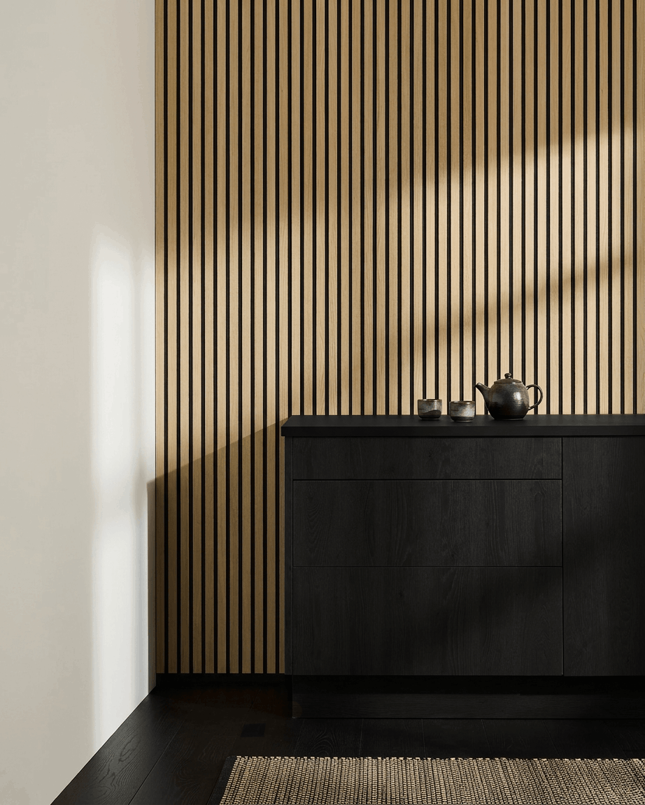 Minimalistiskt nordiskt kök med WoodUpp Akupanel Akustikpanel i Classic Oak, black skåp, tekanna, koppar och vävd matta på mörkt trägolv.