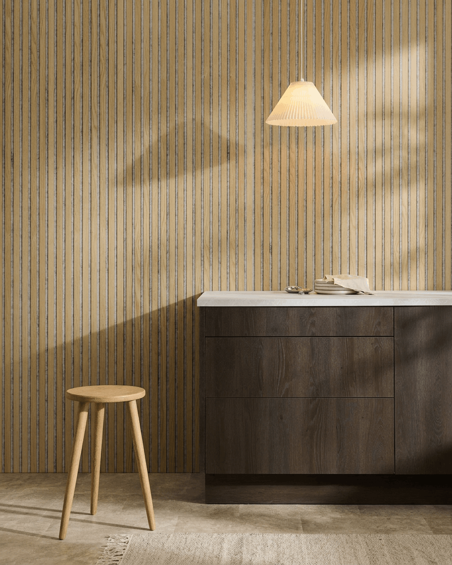Minimalistisk nordisk interiör med en WoodUpp Akupanel Akustikpanel i Classic Oak med Grey filt, kombinerad med en träpall, ett mörkt skåp och en vit bänkskiva.