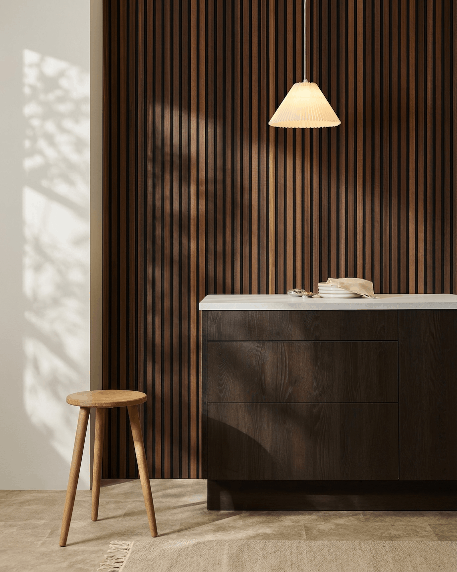Minimalistisk interiör med en träpall, ett mörkt träskåp, en pendellampa och en WoodUpp Akupanel akustisk ribbpanel i Natural Wood/rökt lärk.