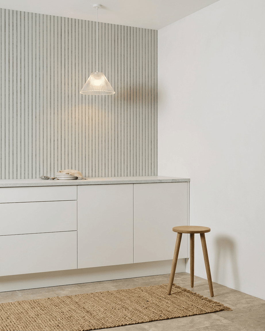 Minimalistiskt kök med vita skåp, träpall, vävd matta och en WoodUpp Akupanel Snow Akustikpanel installerad för ljudabsorption.