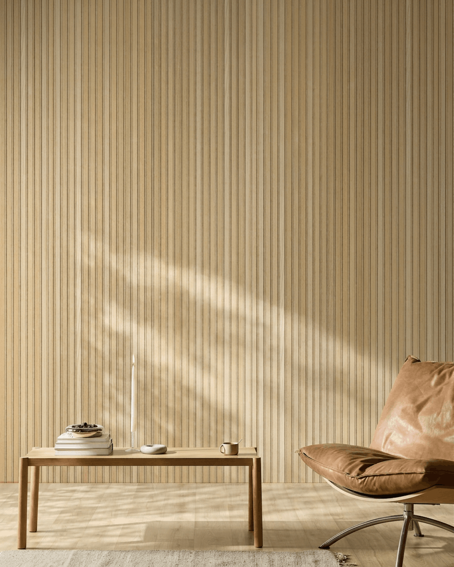 Minimalistiskt skandinaviskt rum med en WoodUpp Akupanel akustikpanel i trä i Natural Wood Classic Oak, en stol i ljusbrunt läder och ett enkelt träbord med ombonade detaljer.