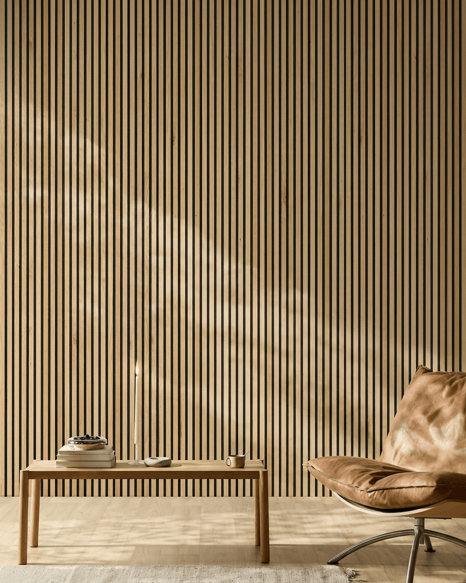 Solljus lyser upp ett modernt rum med en WoodUpp Akupanel Akustikpanel i Rustic Natural Oak på väggen, tillsammans med en ljusbrun läderfåtölj och en minimalistisk bänk.