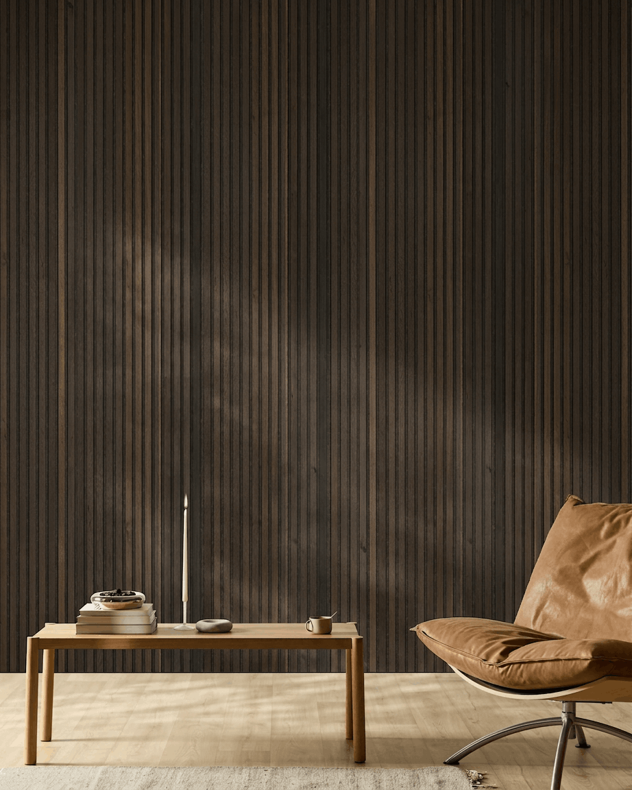 Minimalistiskt nordiskt rum med fåtölj i tanfärgat läder, träbord, ljus och kopp framför en WoodUpp Akupanel Natural Wood Rustic Smoked Oak Akustikpanel vägg.