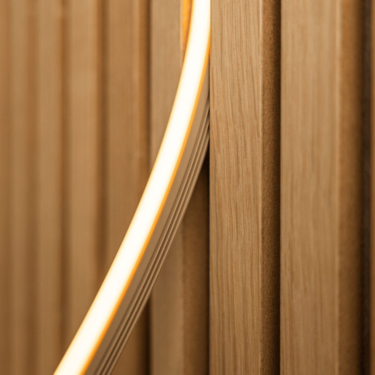 Närbild på WoodUpp Lumi LED-list i beige (240 cm) som avger ett varmt gult ljus över Akupanel vertical akustiska trälameller; kompatibel med Philips Hue.