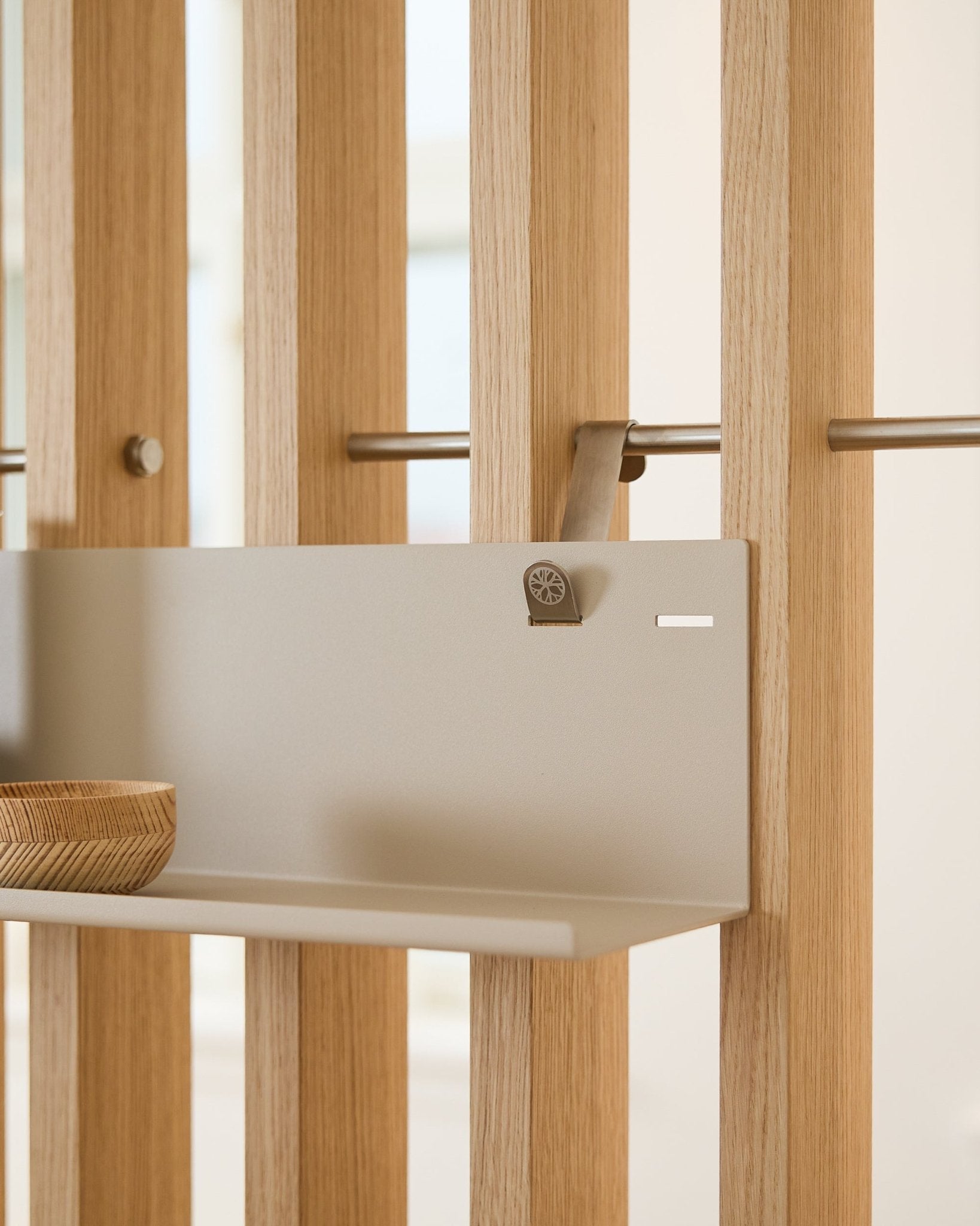 Beige WoodUpp BM1 metallhylla (63x13,4 cm) monterad på vertical akustisk ribbpanel, med en träskål på vänster sida av hyllan.