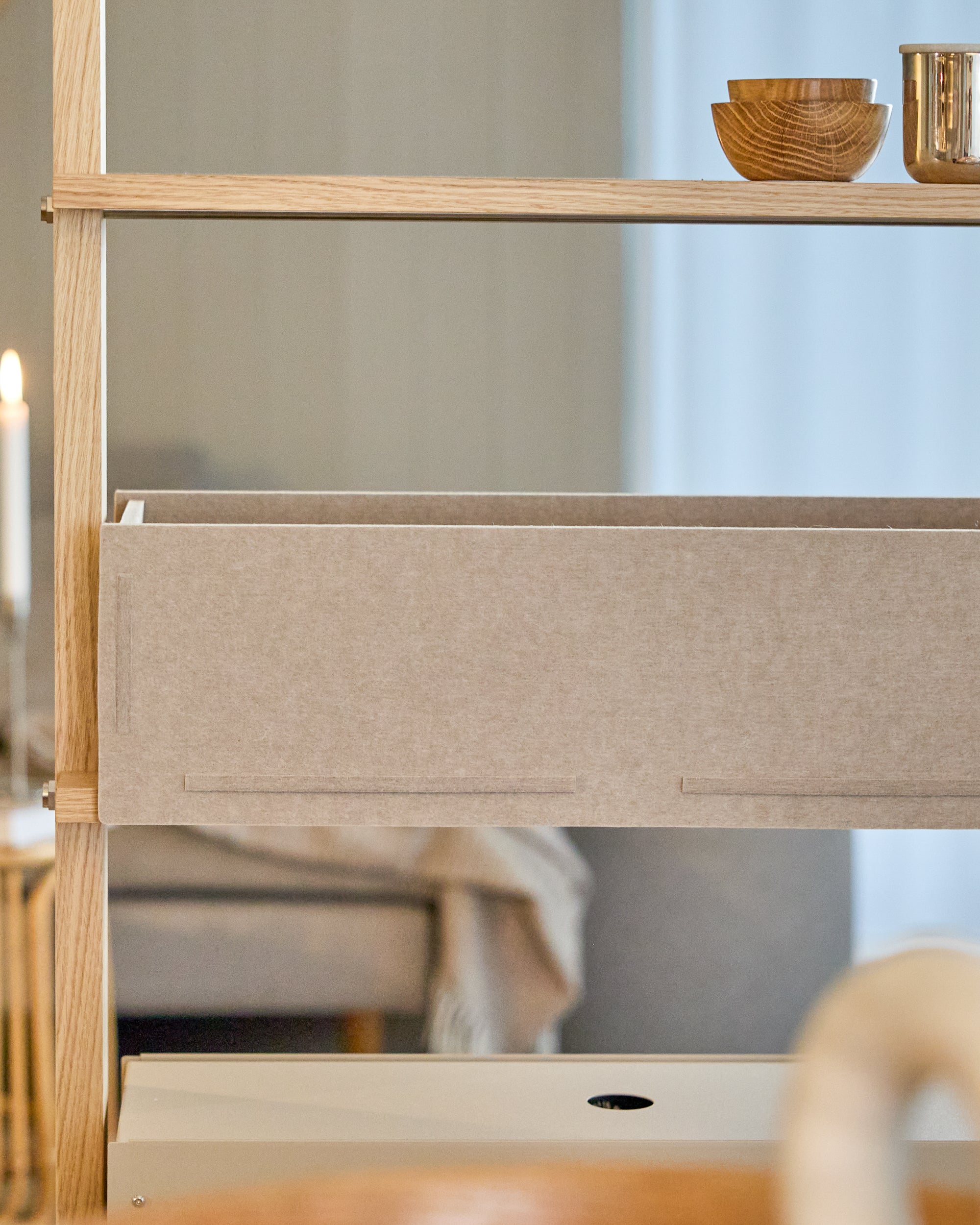 Wooden shelving unit with fabric storage drawer and stacked wooden bowls and metal cup on shelf
