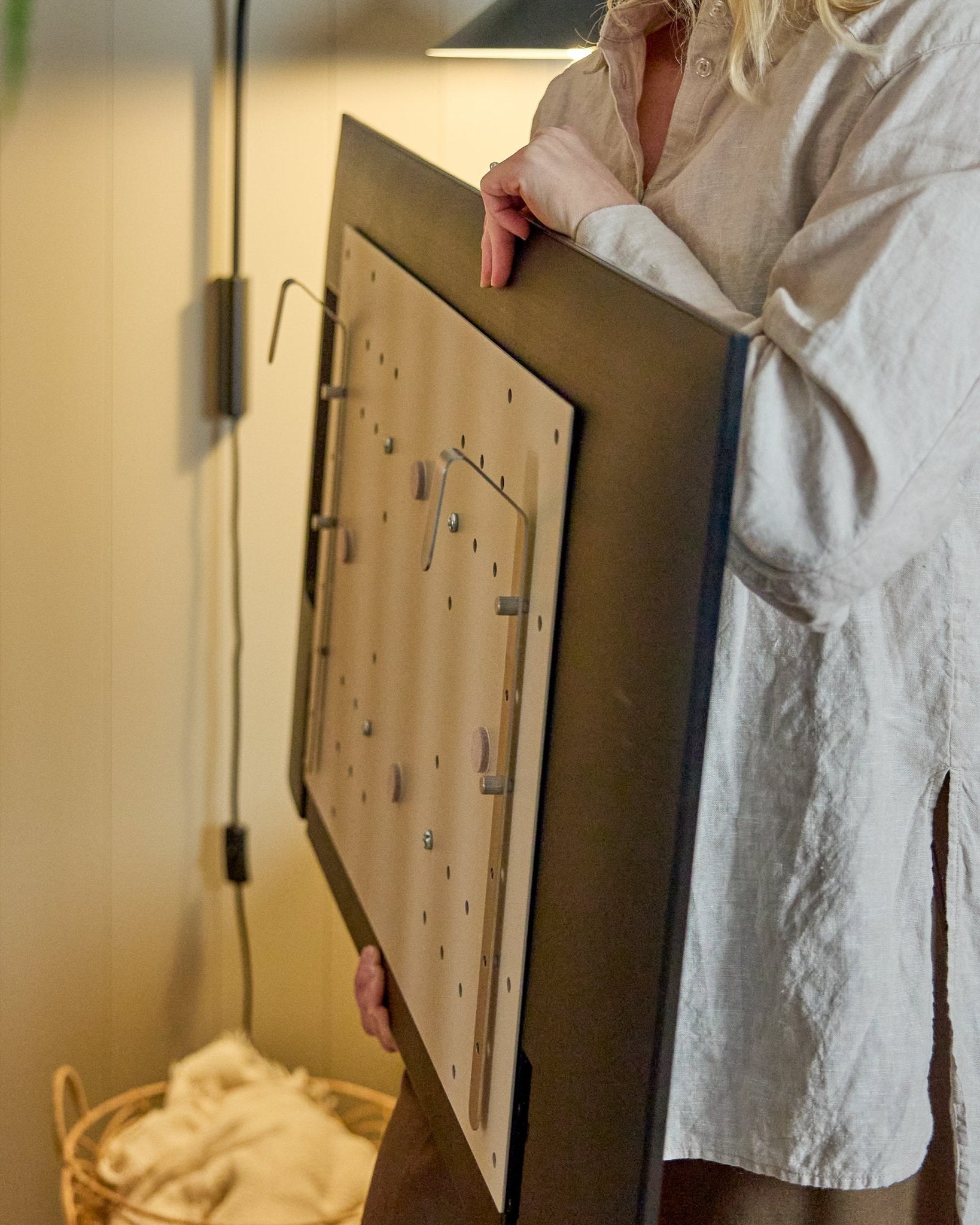 En person i en ljus skjorta håller WoodUpp Nell BM1 TV-Mount i beige, 64x44 cm—kompatibel med nordiska akustikpaneler i trä, för installationer utan vägg.