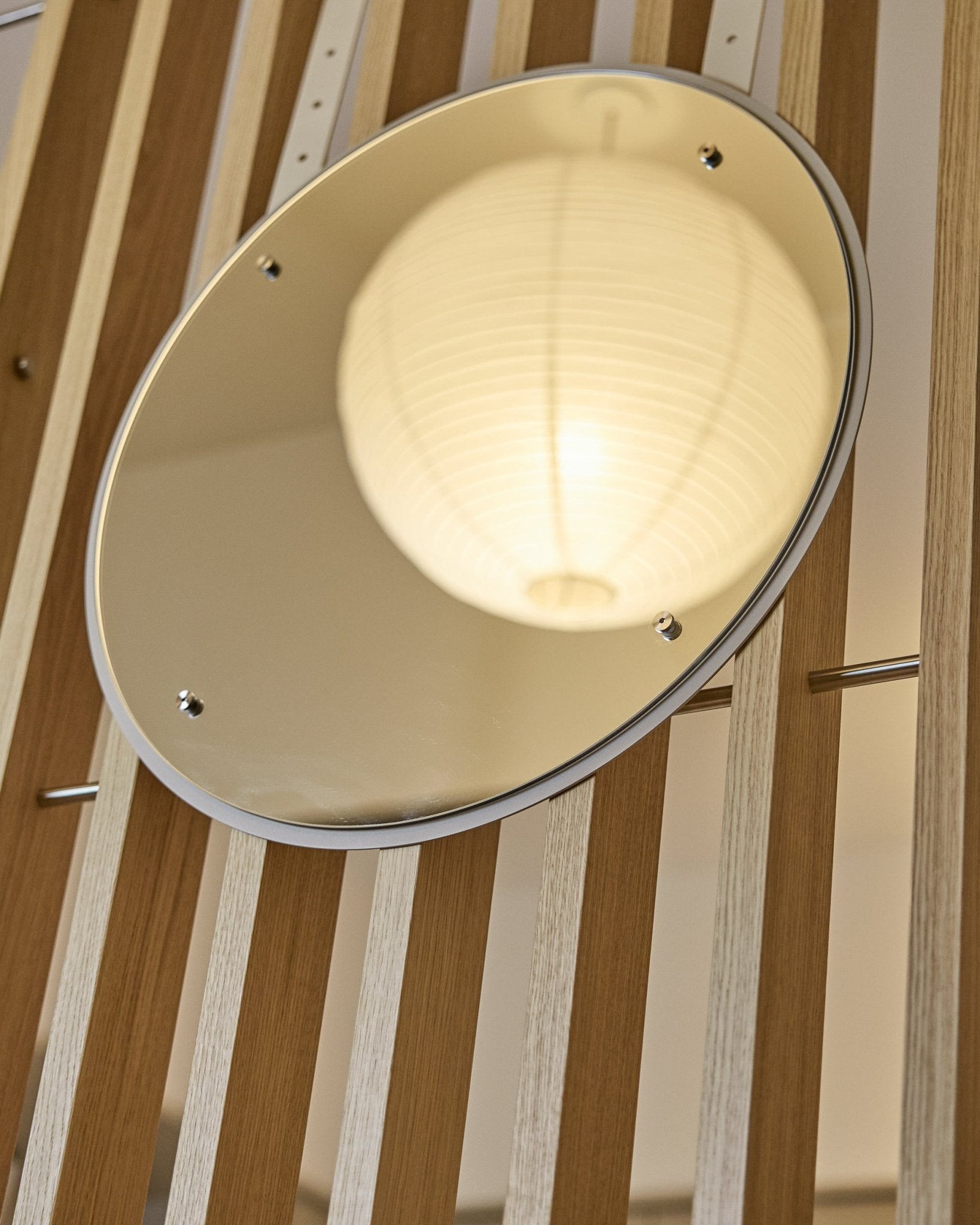 Vala | Mirror / BM1, D54 cm från WoodUpp är en höjdjusterbar rund spegel monterad på vertical akustiska ribbpaneler, där den reflekterar en lysande papperslykta.
