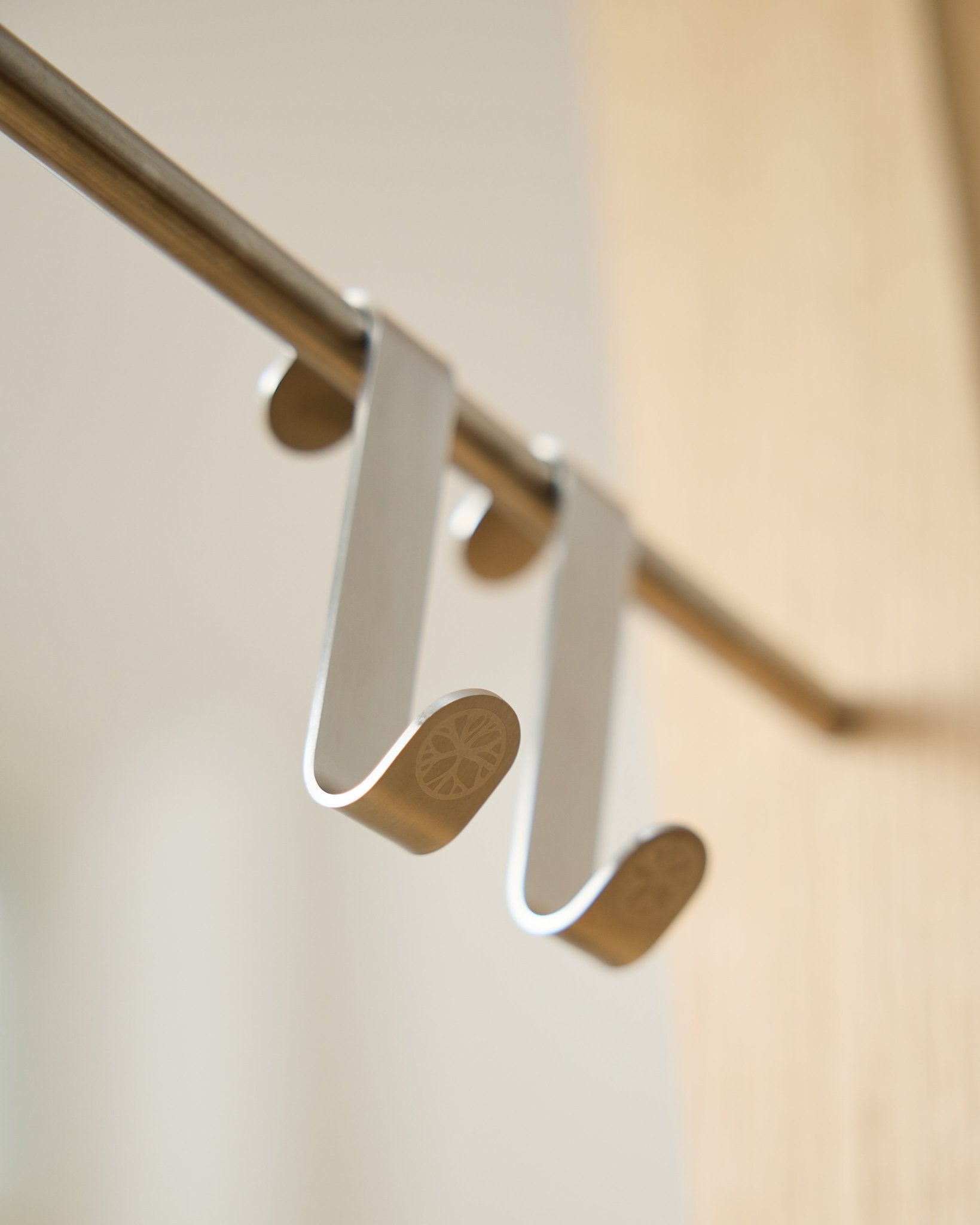 Alva S-krok BM1  BM2 från WoodUpp, två krokar i rostfritt steel med graverade platta ändar, utformade för att hänga upp tillbehör på Akupanel horizontal stänger.