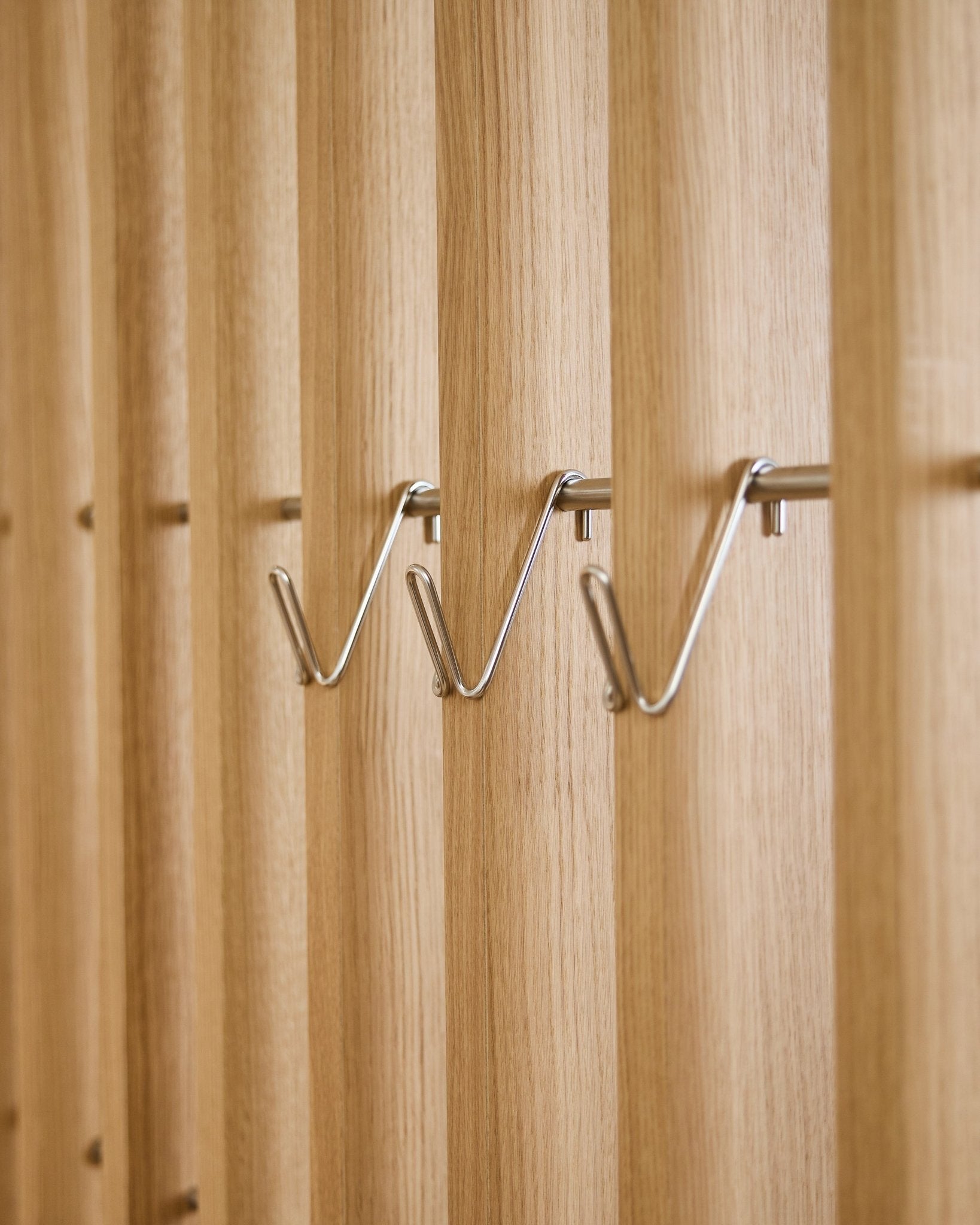 Tre korta Alva Wire Hook / BM1-tillbehör i rostfritt steel från WoodUpp är jämnt monterade i rad på en vertical akustikpanel med trälameller.