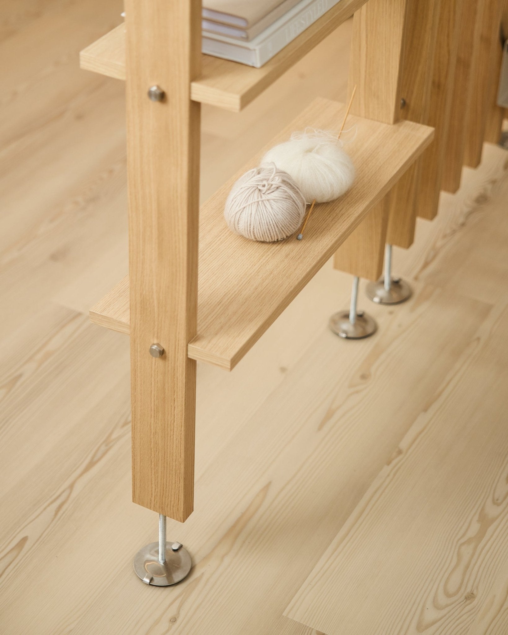 Lova | Wood Shelf / BM2 från WoodUpp i ekfaner (65,8 x 20 cm), med garn och stickor på den nedre hyllan, på ett ljust trägolv med metallfötter.