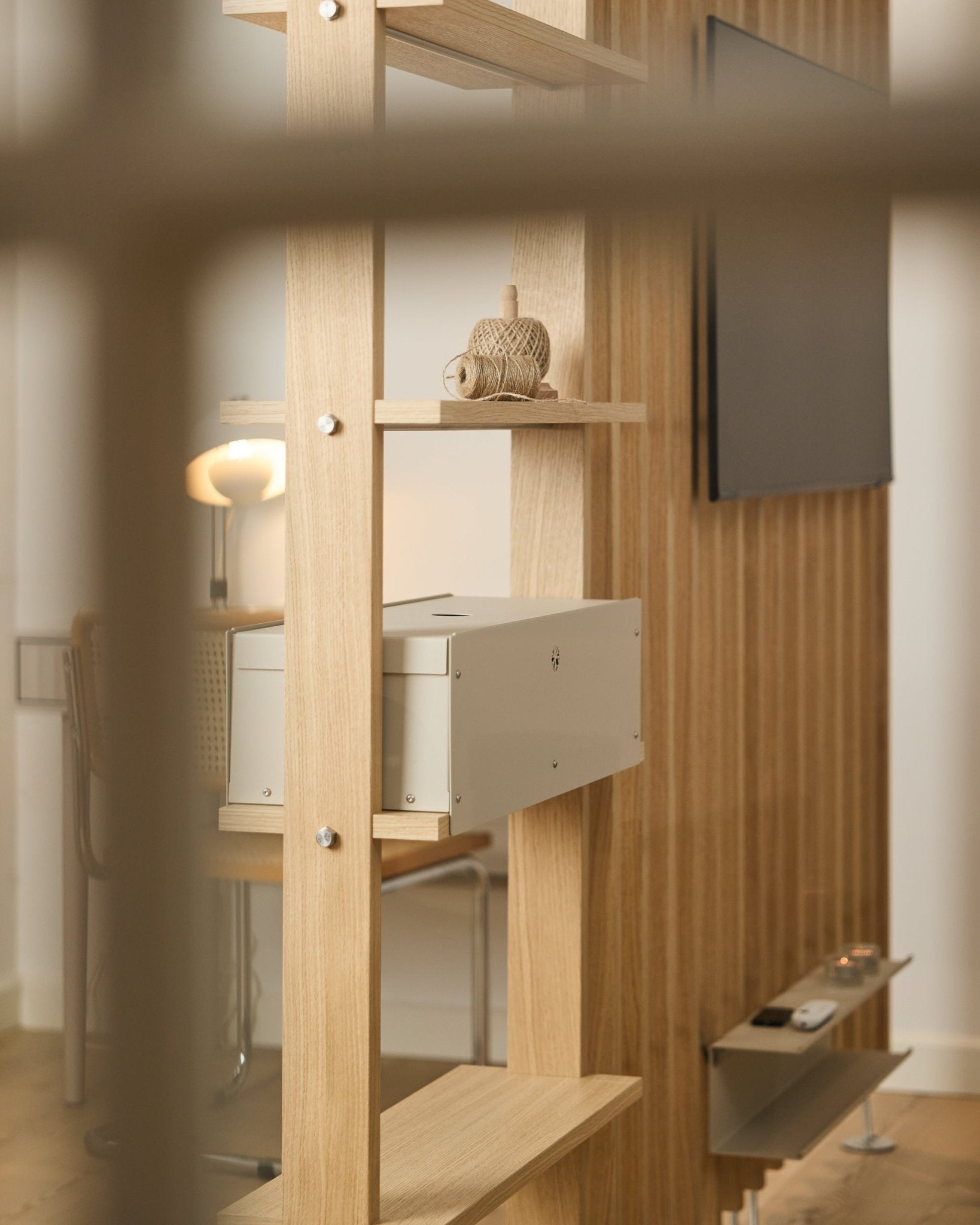 Ett ombonat rum med stol, lampa och TV visar hyllan Nell | Metal Box / BM2 från WoodUpp, i beige, med minimalistisk nordisk inredning.