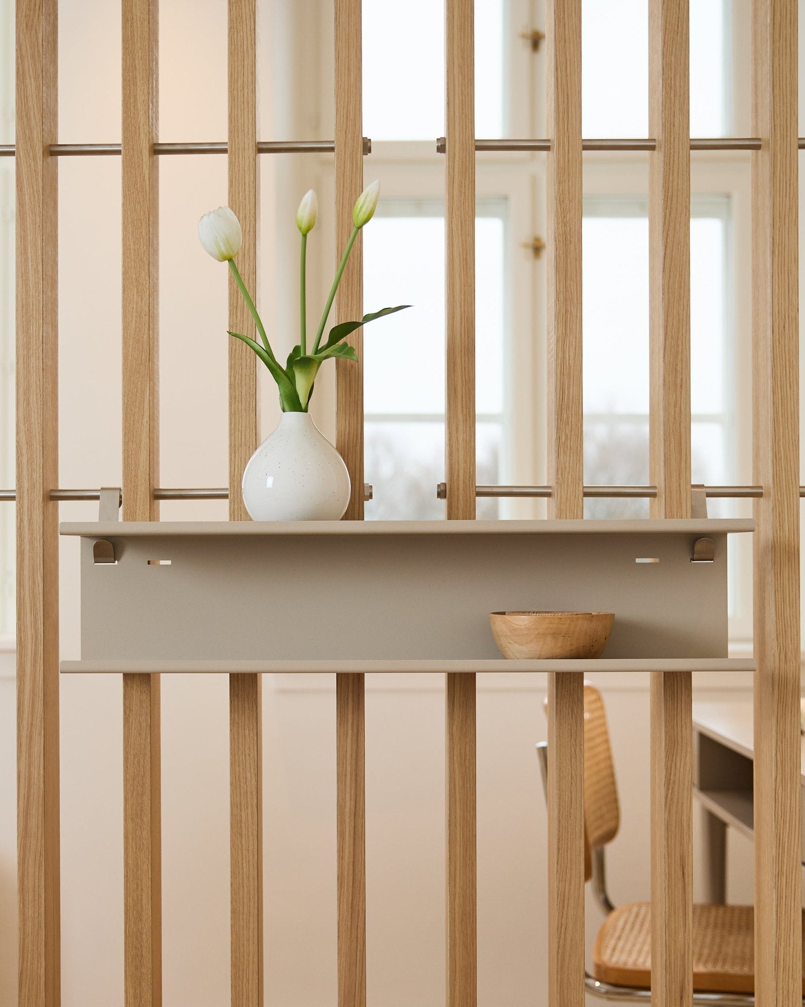 Double Metal Shelf / BM1 från WoodUpp i beige (63,5 cm), monterad på en ribbad rumsavdelare och stylad med en vas och en träskål.