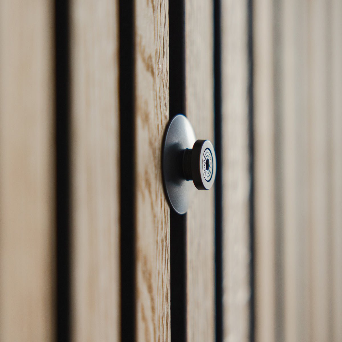 Närbild av Dupps | Heavy titthål från WoodUpp i black aluminium, monterat på en räfflad trädörr med Akupanel akustiklameller, med linsen i fokus.