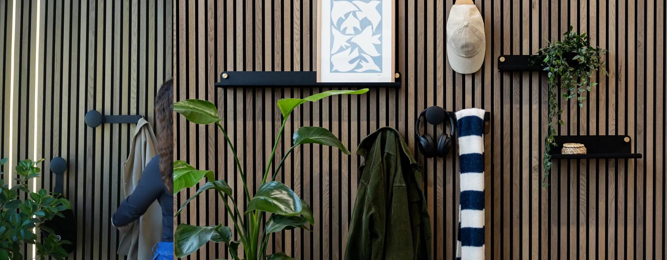 En man i blå jacka går förbi en nordisk Akupanel akustisk träribbvägg med integrerade växter, hyllor, klädkrokar, hörlurar och en hoprullad randig handduk.