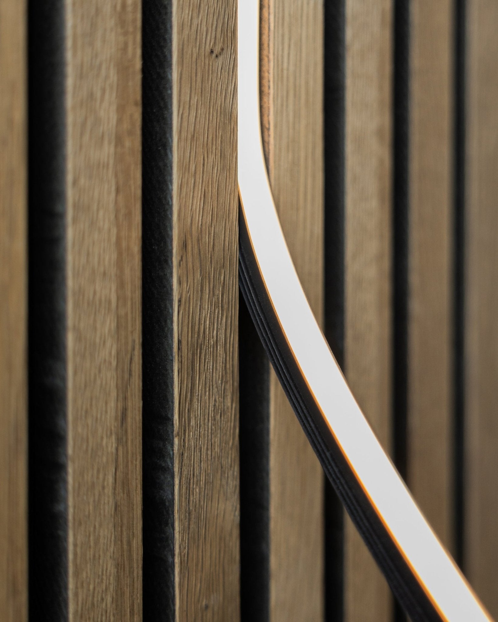 Närbild av WoodUpp Akupanel Akustikpanel i natural wood finish med black spår och en 300 cm Lumi LED-list som skapar ett modernt, linjärt mönster.
