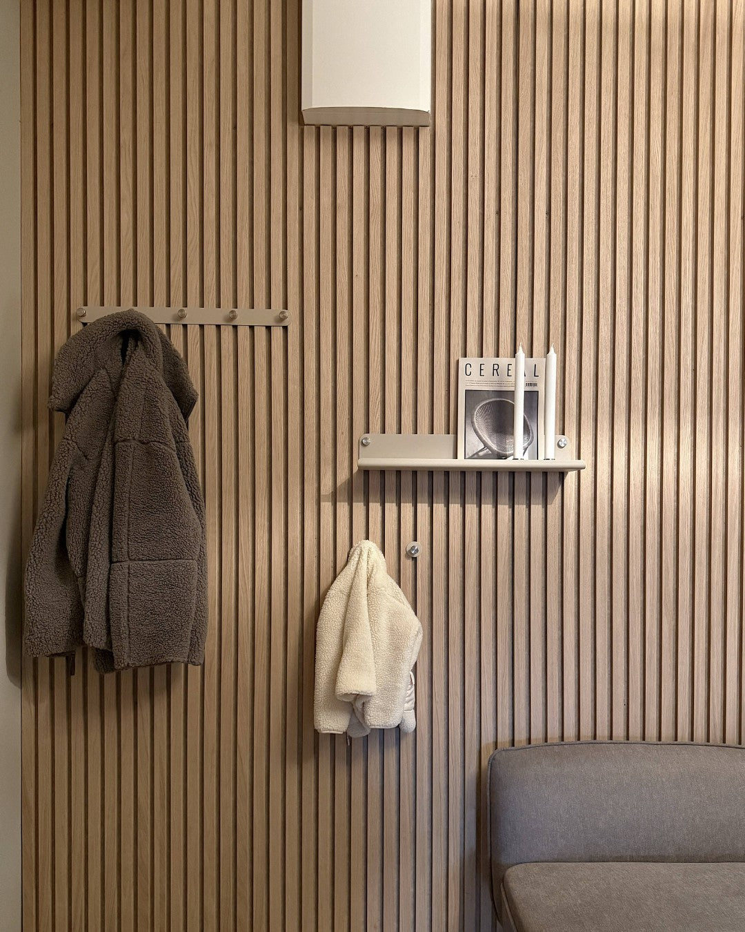 Wall with slatted design, coat rack, and shelf with books against a neutral wall.