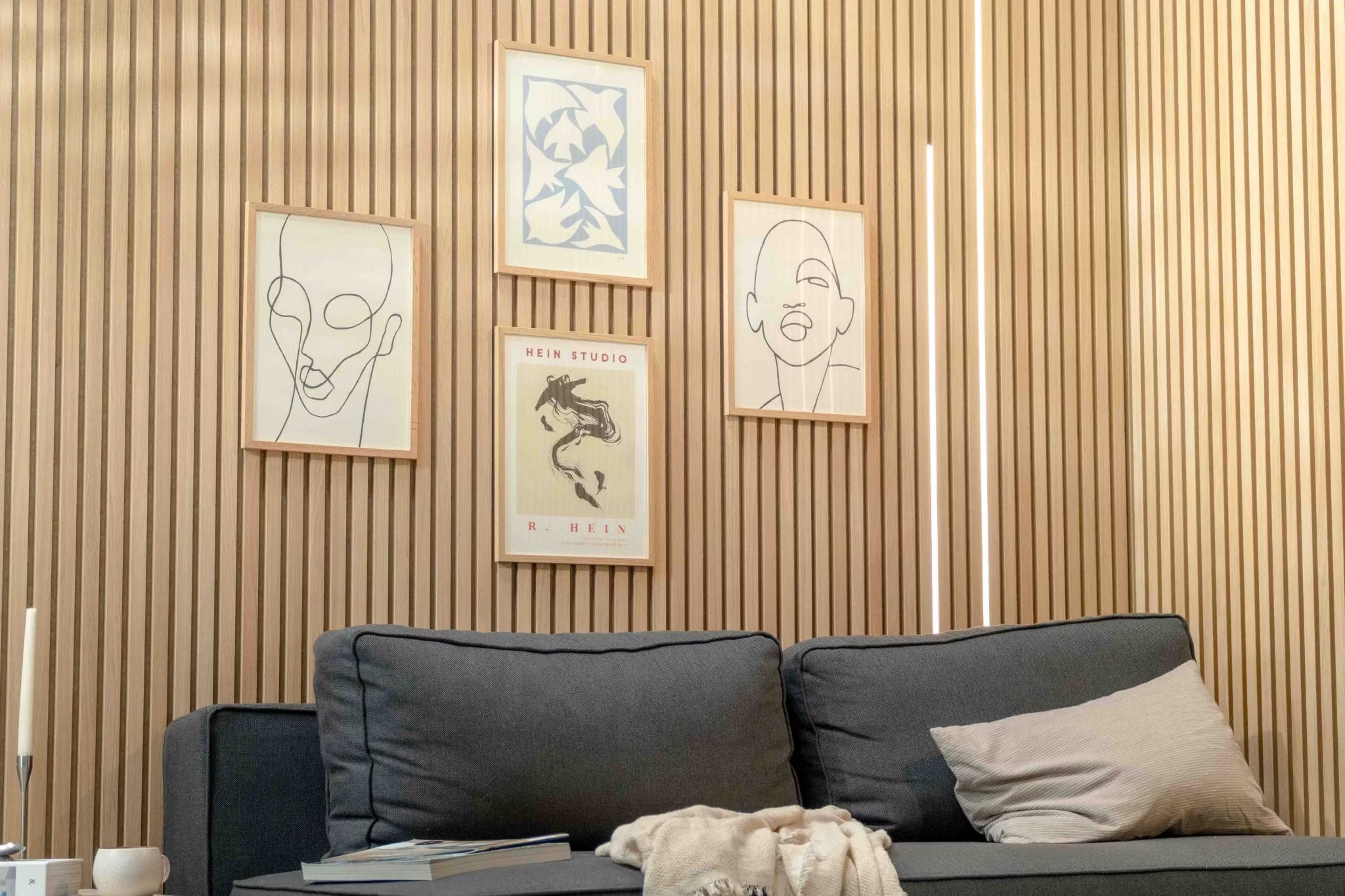 Modernt vardagsrum med en mörk soffa med en beige kudde, accentuerad av en nordisk Akupanel akustisk träribbvägg och minimalistisk skandinavisk konst ovanför.