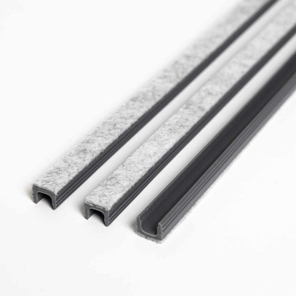 Produktbild från WoodUpp: tre grå U-formade plastprofiler för tätning, presenterade i olika varianter. Två profiler har ljusgrå filt fastsatt på ovansidan, den tredje har filt under profilen. Noga skurna ändar visar kanalens form, stadga och filtens mjuka textur och ytkvalitet.