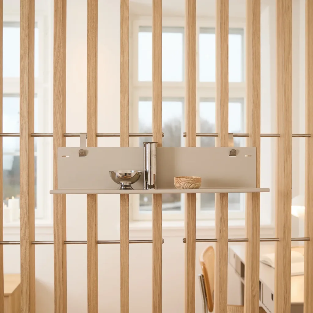 WoodUpp rumsavdelare i ljust trä med monterad beige hylla/panel från WoodUpp, stilren och modulär, fäst med synliga metallclips och stänger. På hyllan står en hög blank metallvas, en liten rostfri skål och en rund träskål, perfekt för förvaring och dekoration.